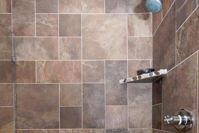Shower stall with brown and beige textured tiles and a built-in shelf.