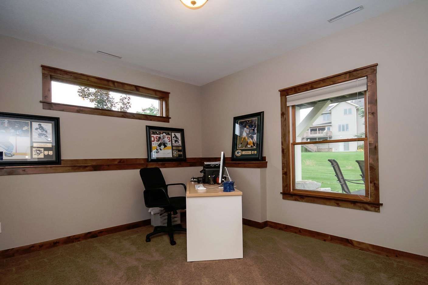 Home office with a desk, black chair, and framed pictures on tan walls.