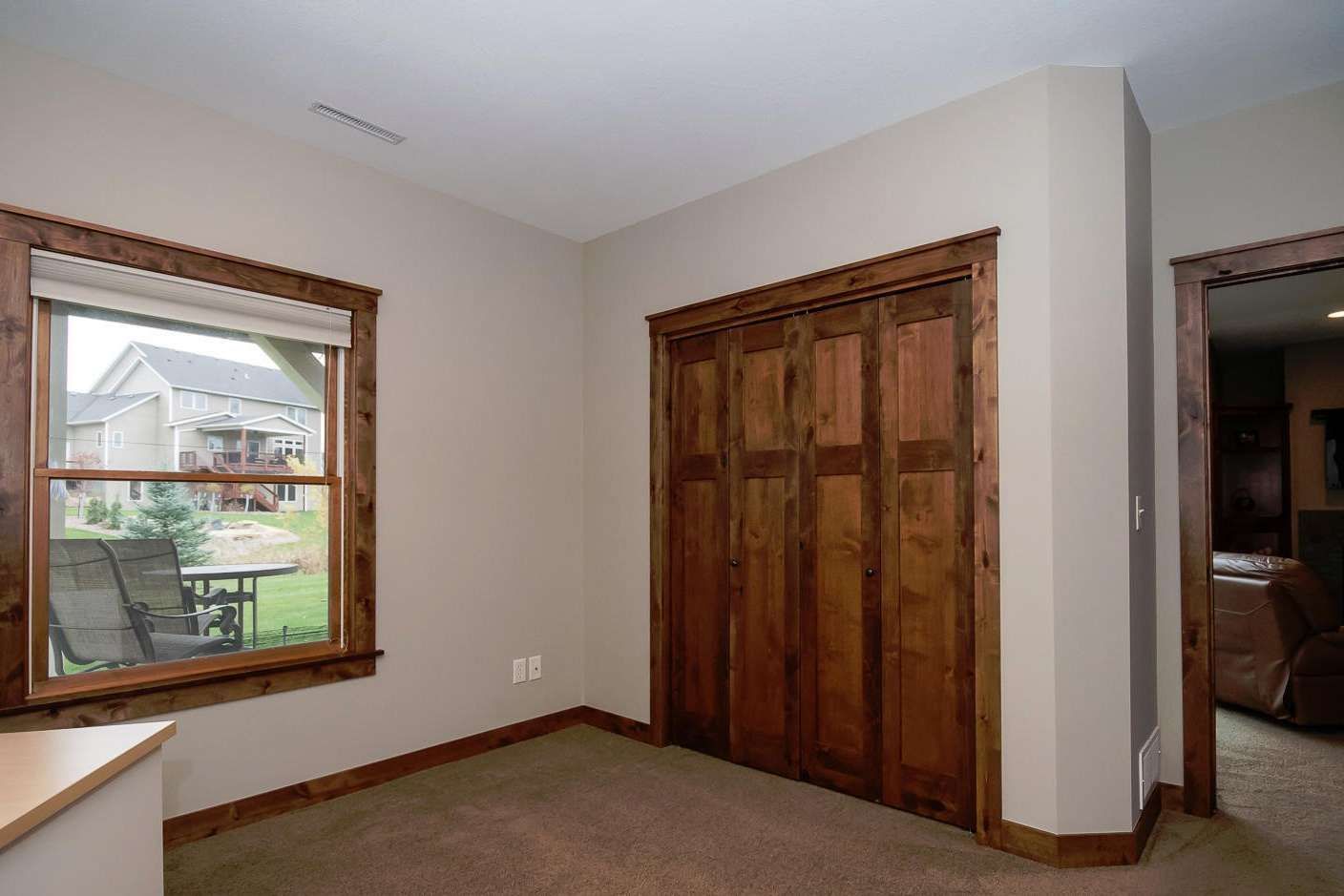 Bedroom with wooden-framed window and closet doors, beige walls, and brown trim.