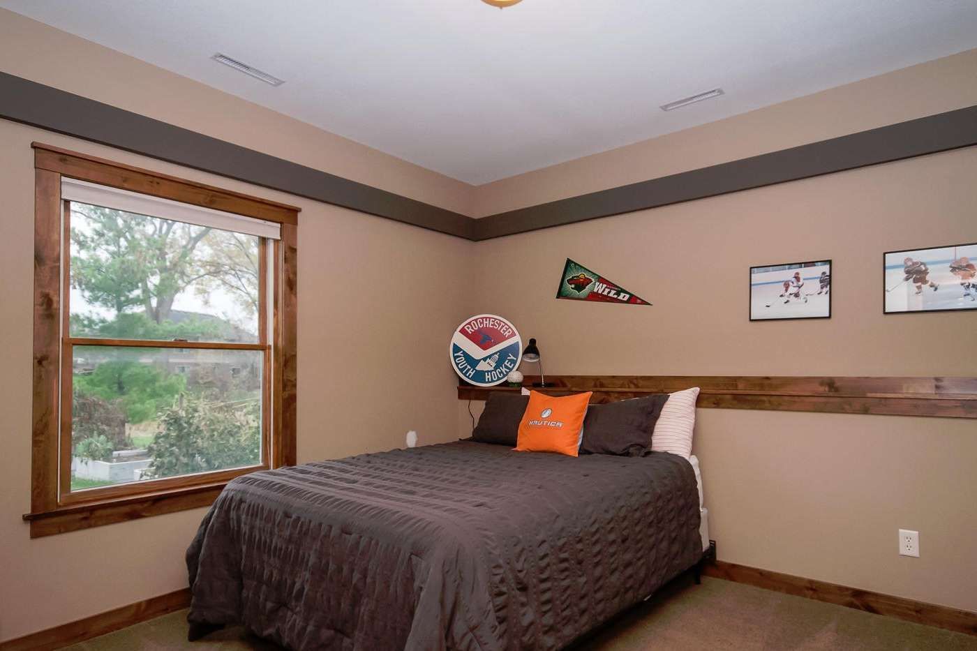 Bedroom with bed, window, sports decor, and brown walls.