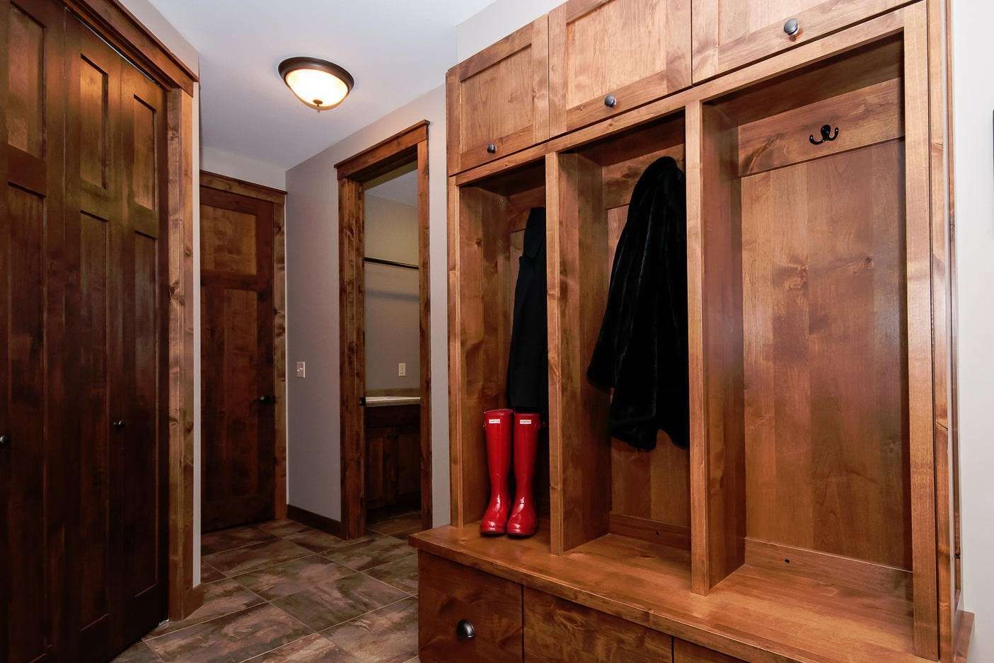 Wooden entryway with built-in storage, coats, and red boots. Doorways lead to other rooms.