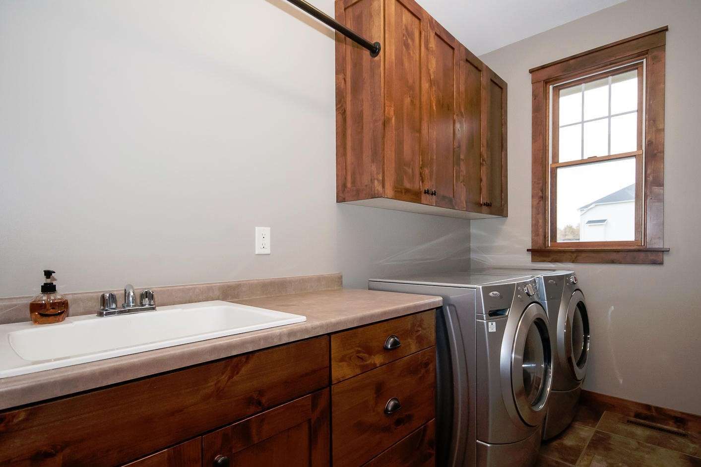 Laundry room with wood cabinets, countertop, sink, and washer/dryer. Small window to the right.
