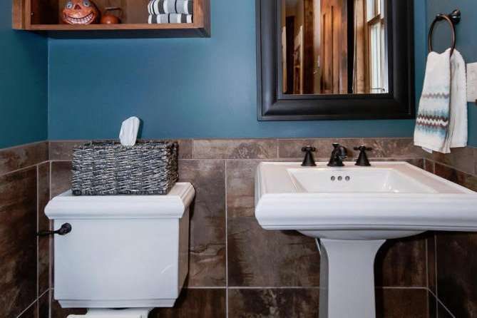 Small bathroom with dark blue wall, brown tile, white pedestal sink, and toilet.