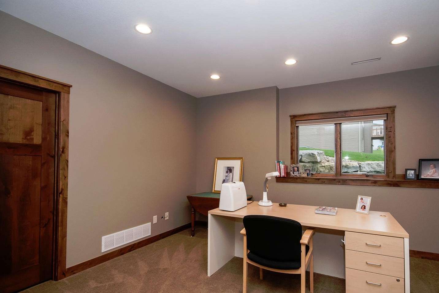 Home office with tan walls, desk, chair, window, and wood door.