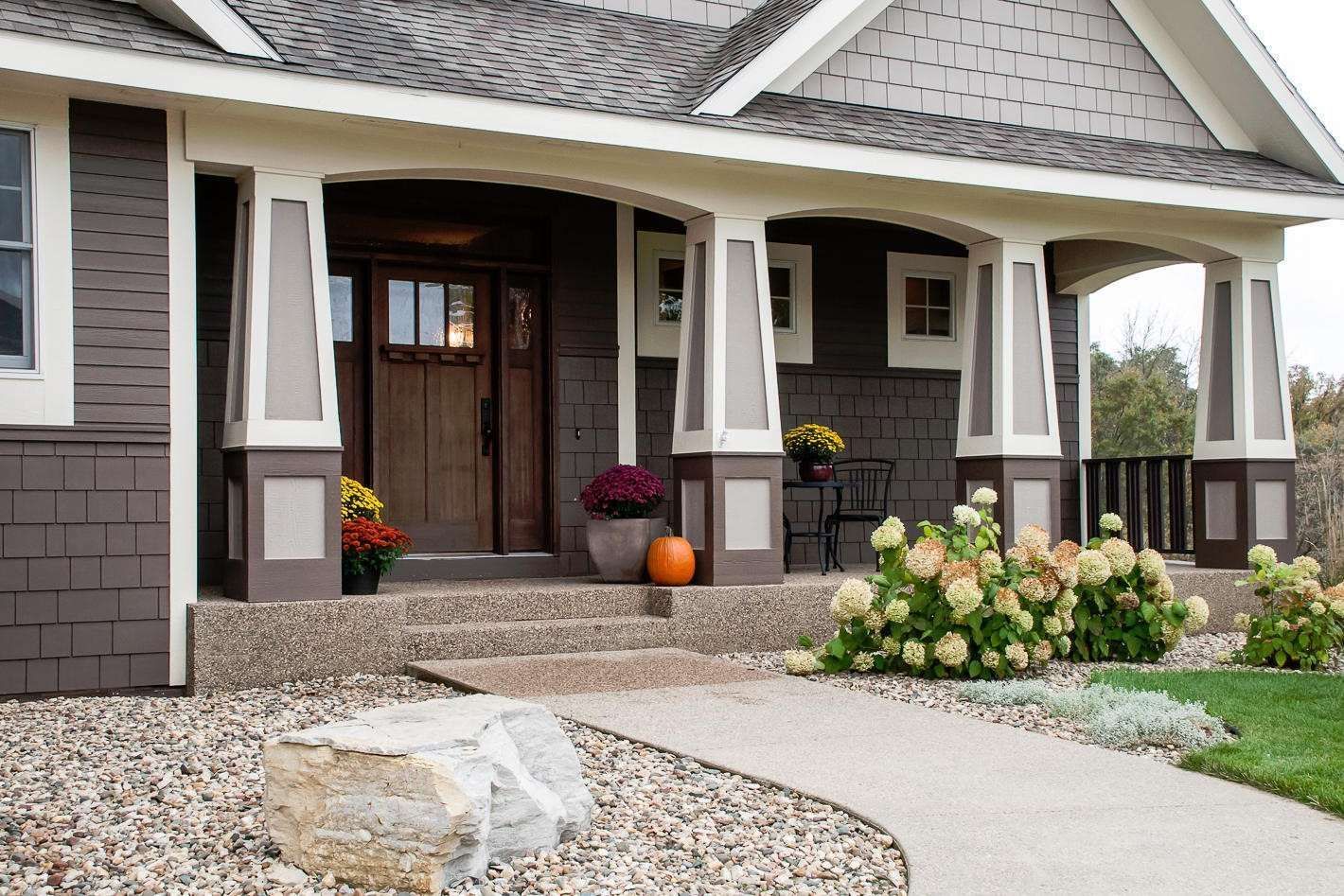Brown house with porch, walkway, landscaping, and steps leading to the front door.