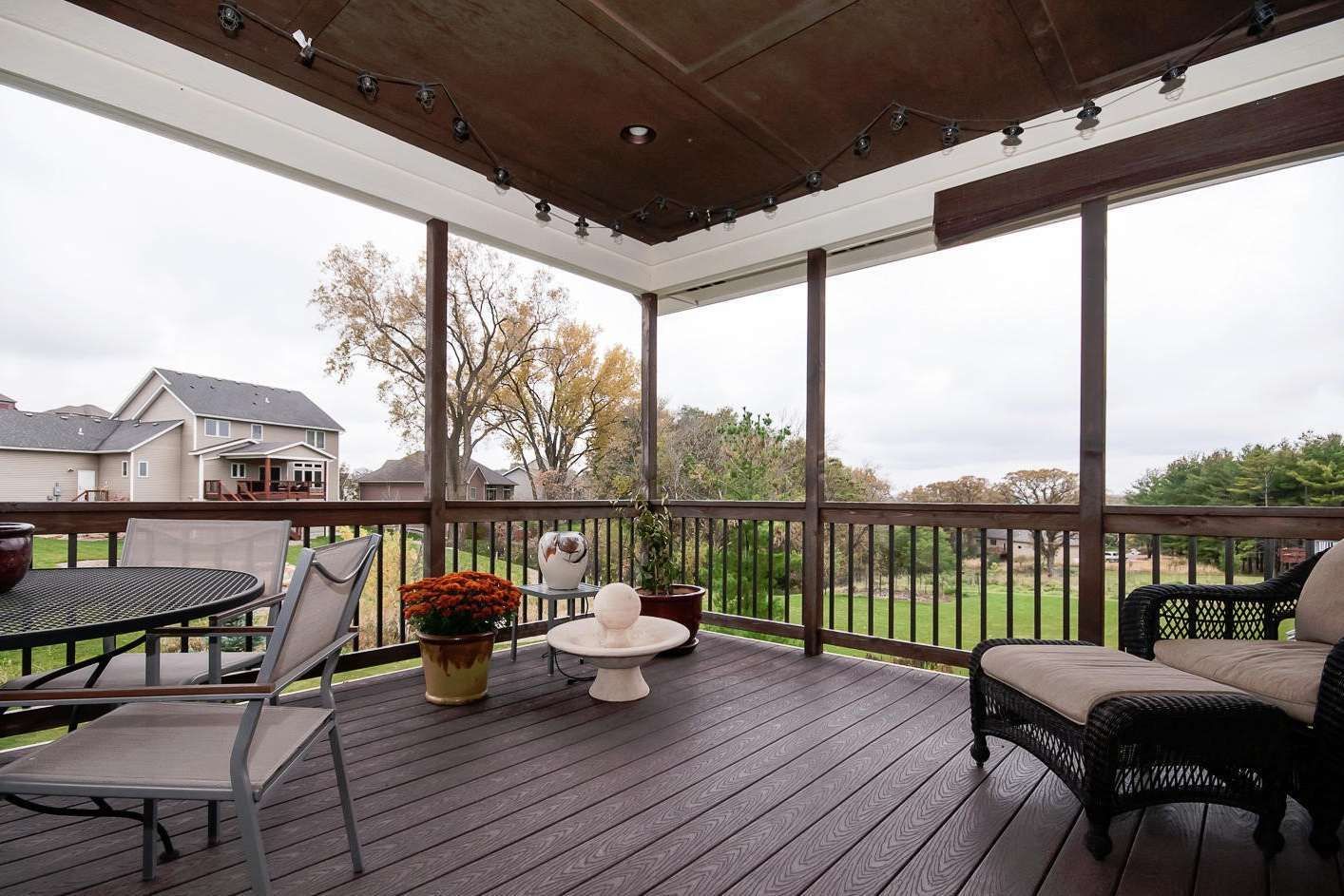 Screened-in porch with dark wood deck, seating, and view of houses and trees under an overcast sky.