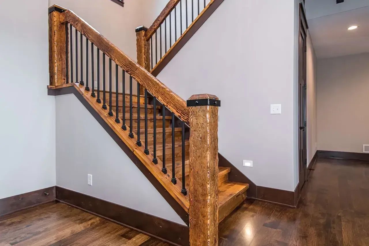 Wooden staircase with black metal balusters, dark brown wood floor, light gray walls.
