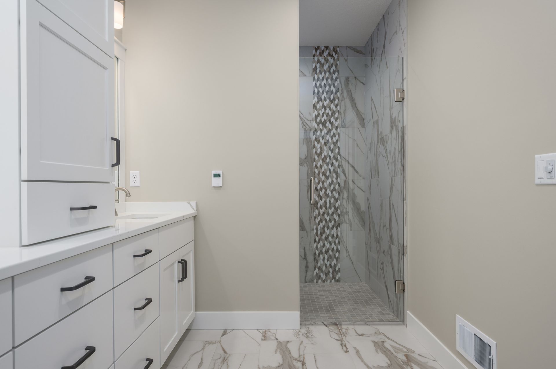 Modern bathroom with white vanity, marble shower, and beige walls.