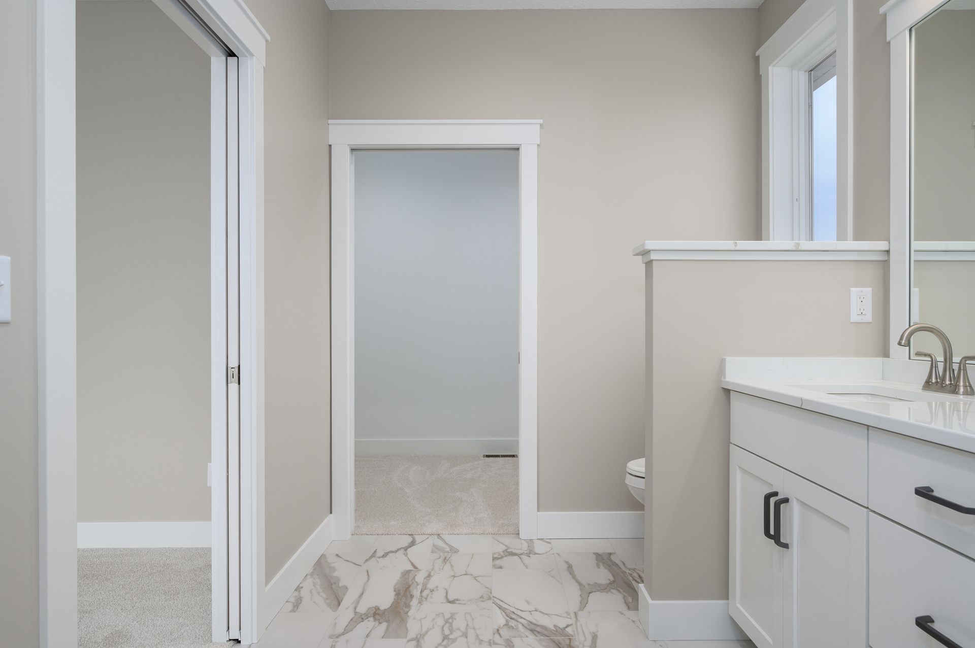 Bathroom with white cabinets, marble floor, and doorways with white trim.