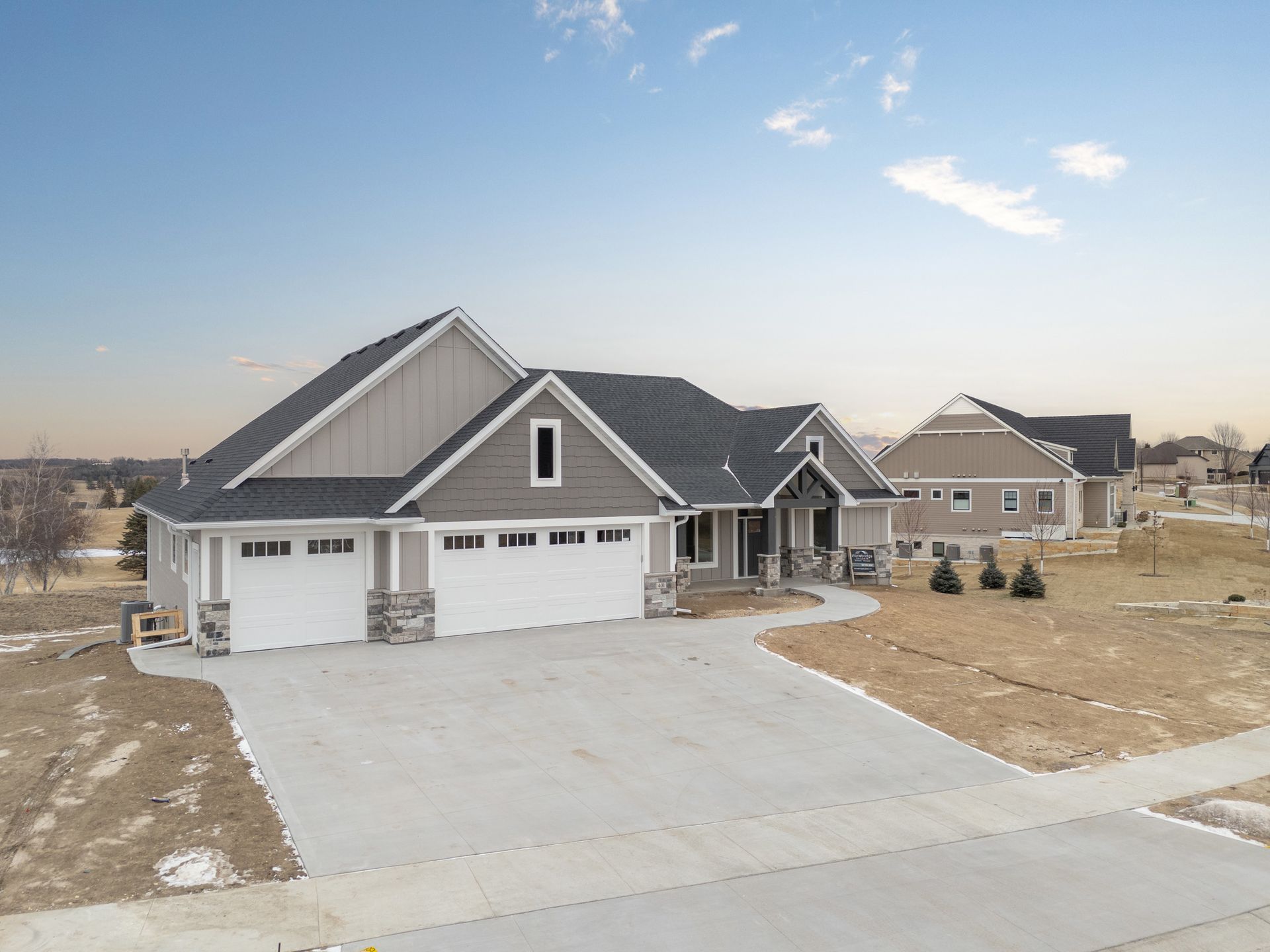 Modern beige house with a three-car garage and concrete driveway under a partly cloudy sky.