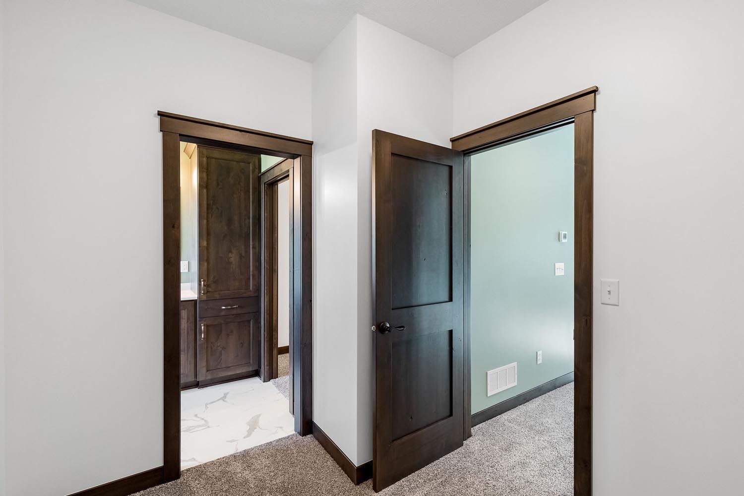 Interior hallway with three dark wooden doors framed by dark trim, white walls, and carpet.