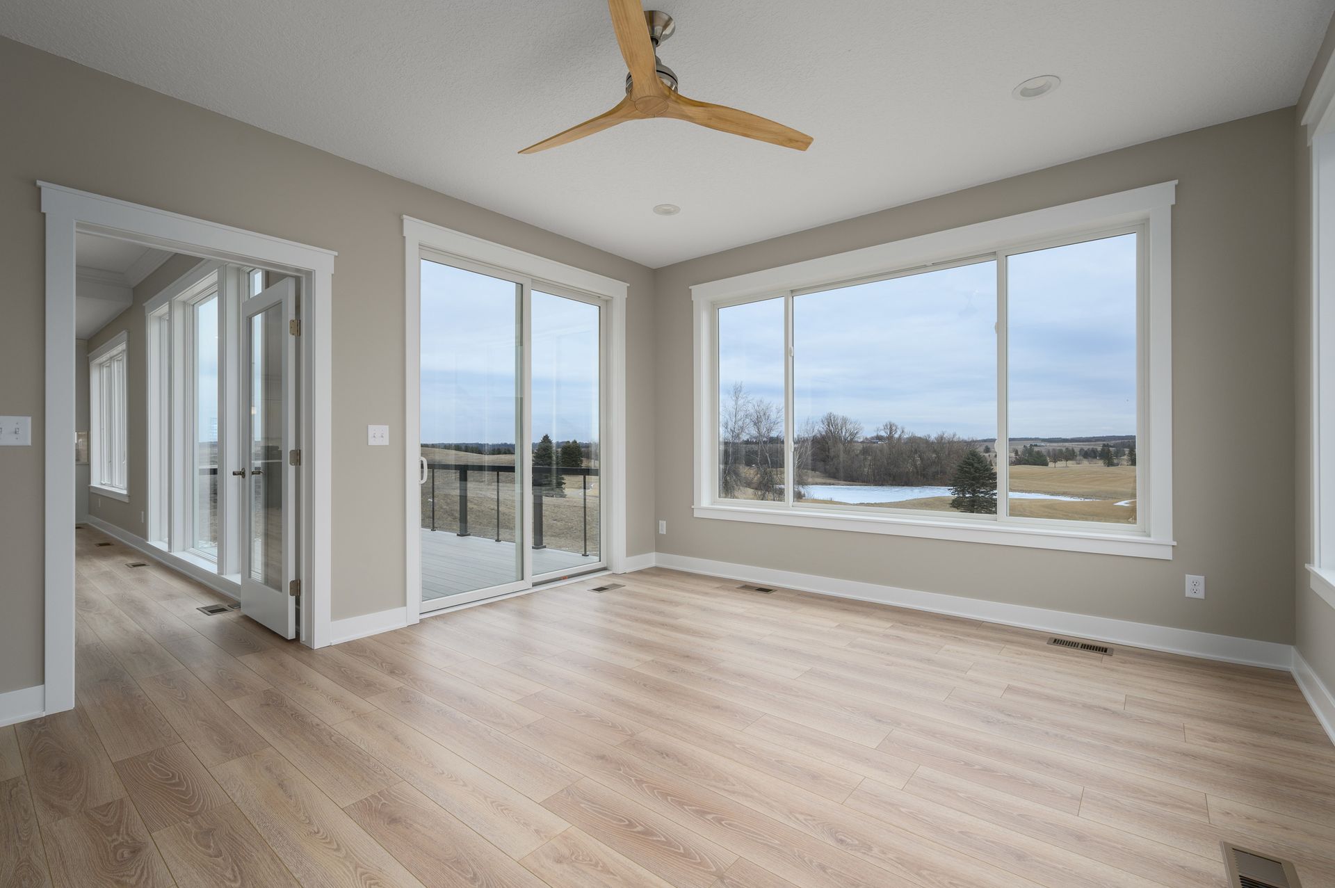 Empty room with light wood floors, large windows with a view, and a ceiling fan.