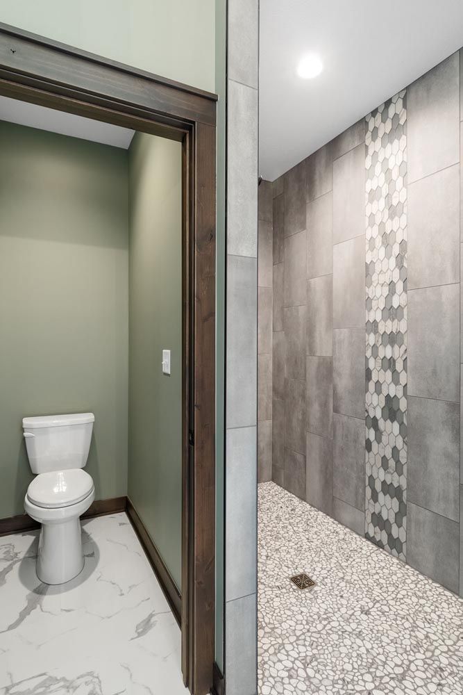 Bathroom with toilet visible through doorway; shower with pebble floor and gray tile.
