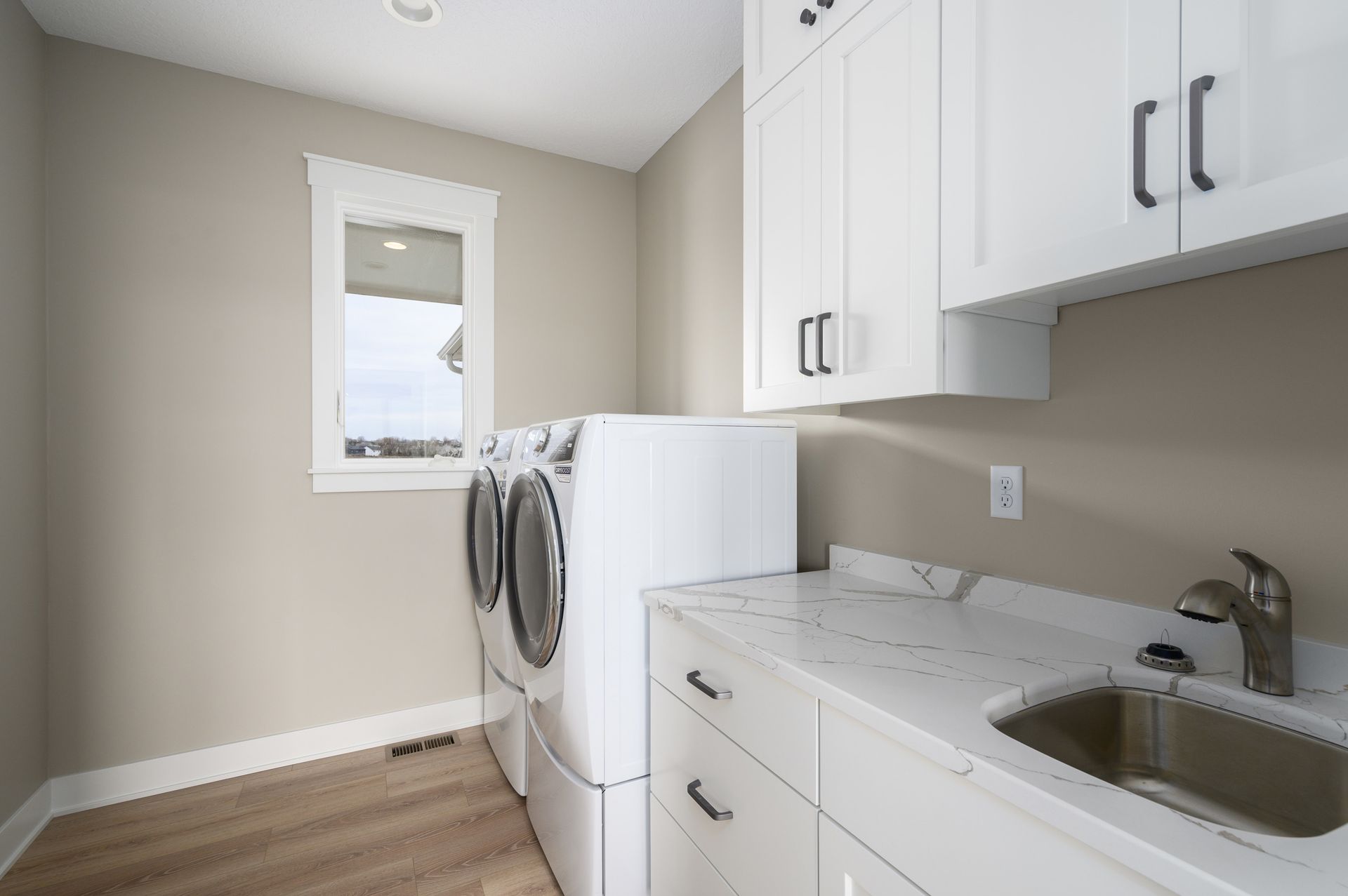 Laundry room with white cabinets, washer/dryer, sink, and window.