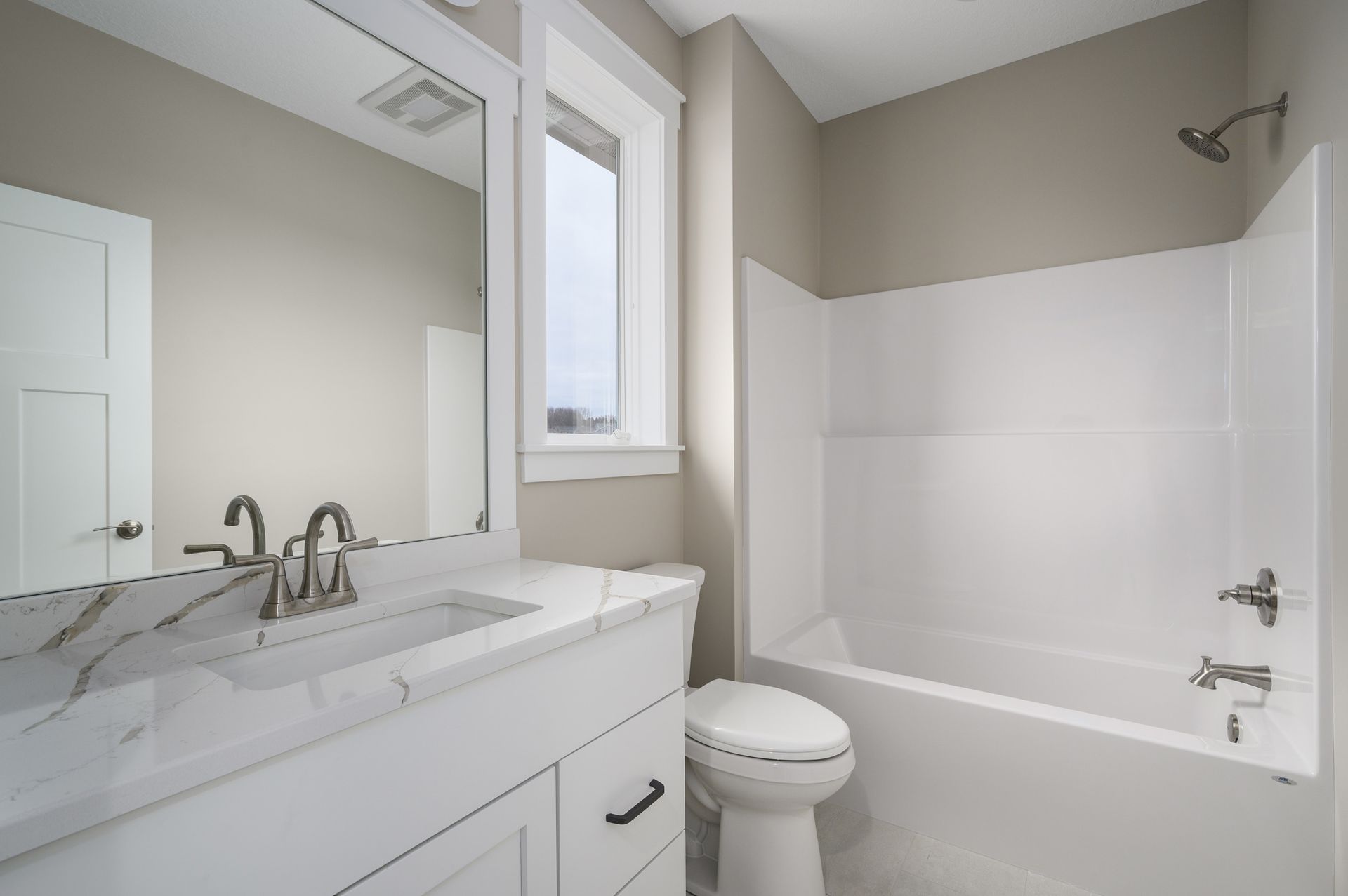 Bathroom with white fixtures, vanity, toilet, and bathtub. Beige walls and a small window.