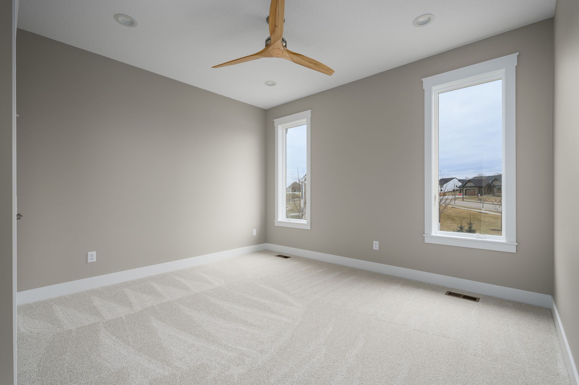 Empty bedroom with neutral walls, white trim, two windows, and beige carpet.