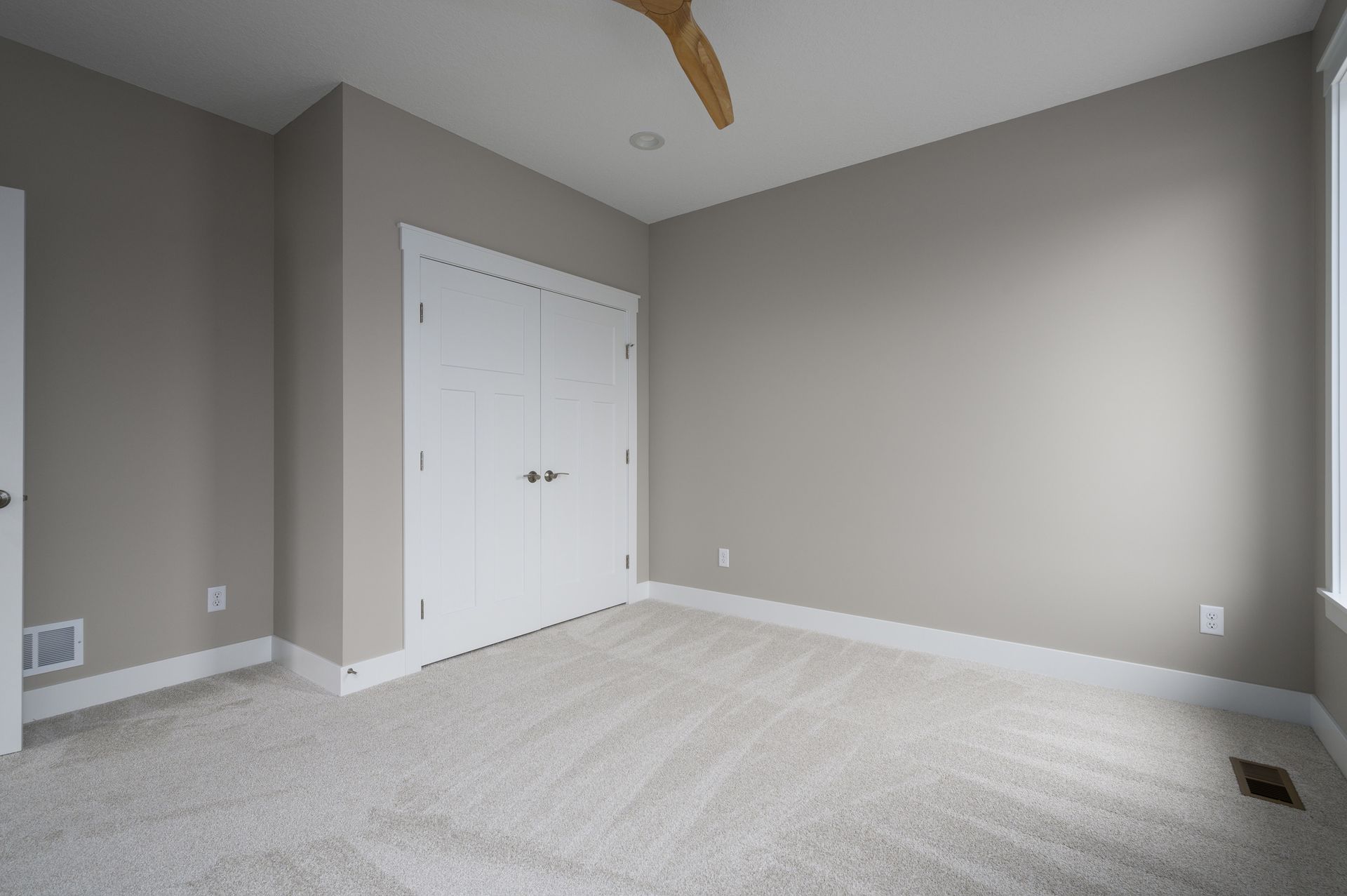 Empty room with beige carpet, light gray walls, white closet doors, and a ceiling fan.