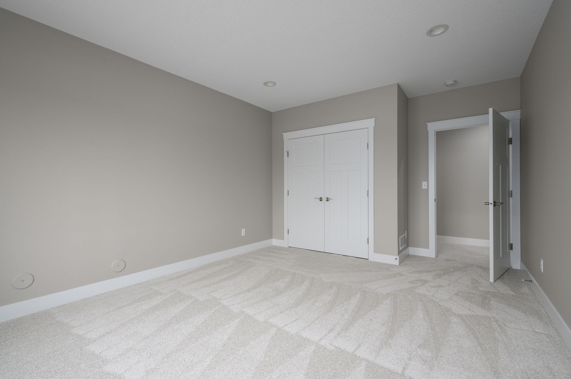 Empty bedroom with light gray walls, white trim, and carpet, with closed closet doors and open doorway.