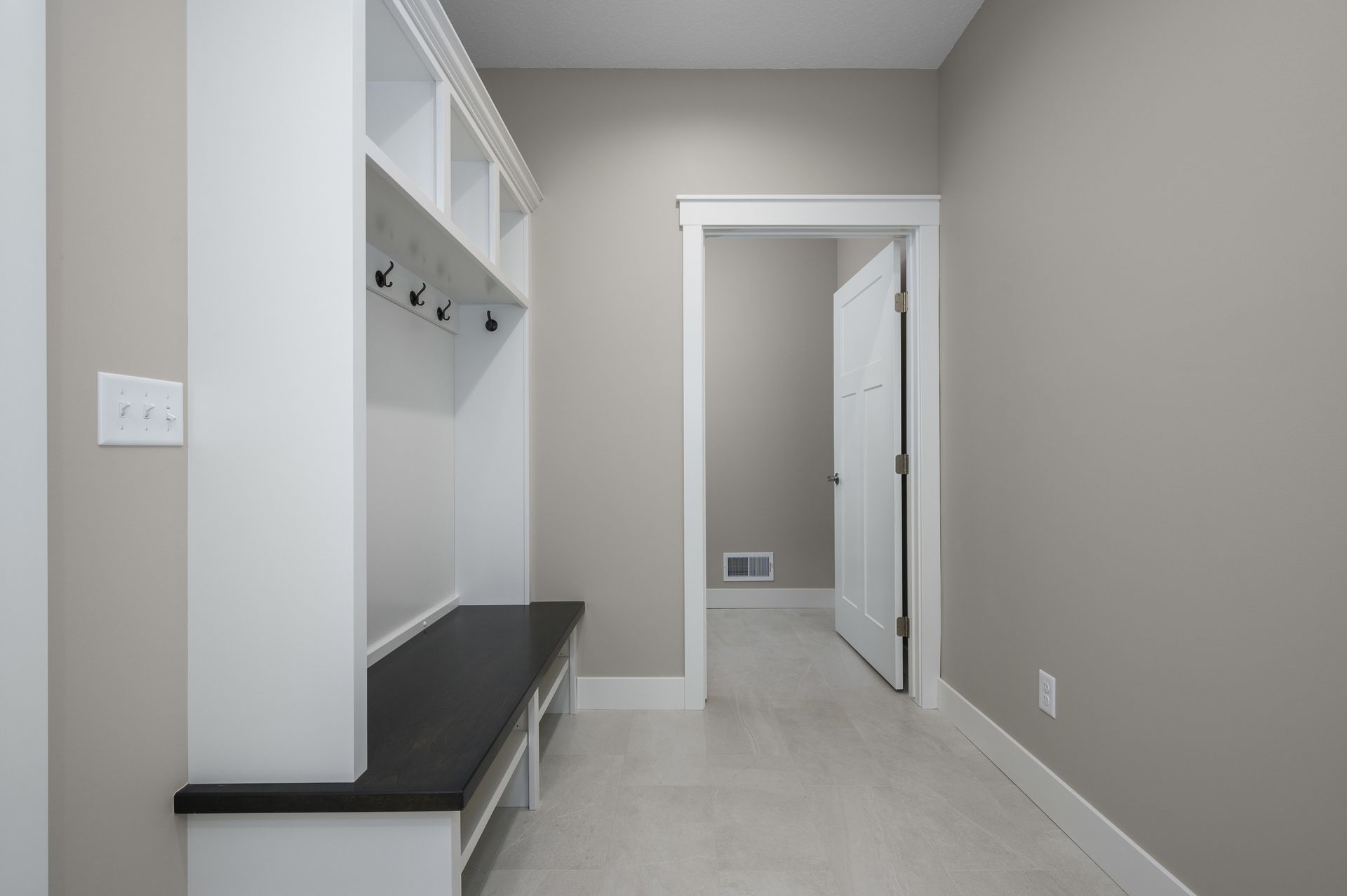 Mudroom with white built-in storage bench, hooks, and open shelving, gray walls, and open door.