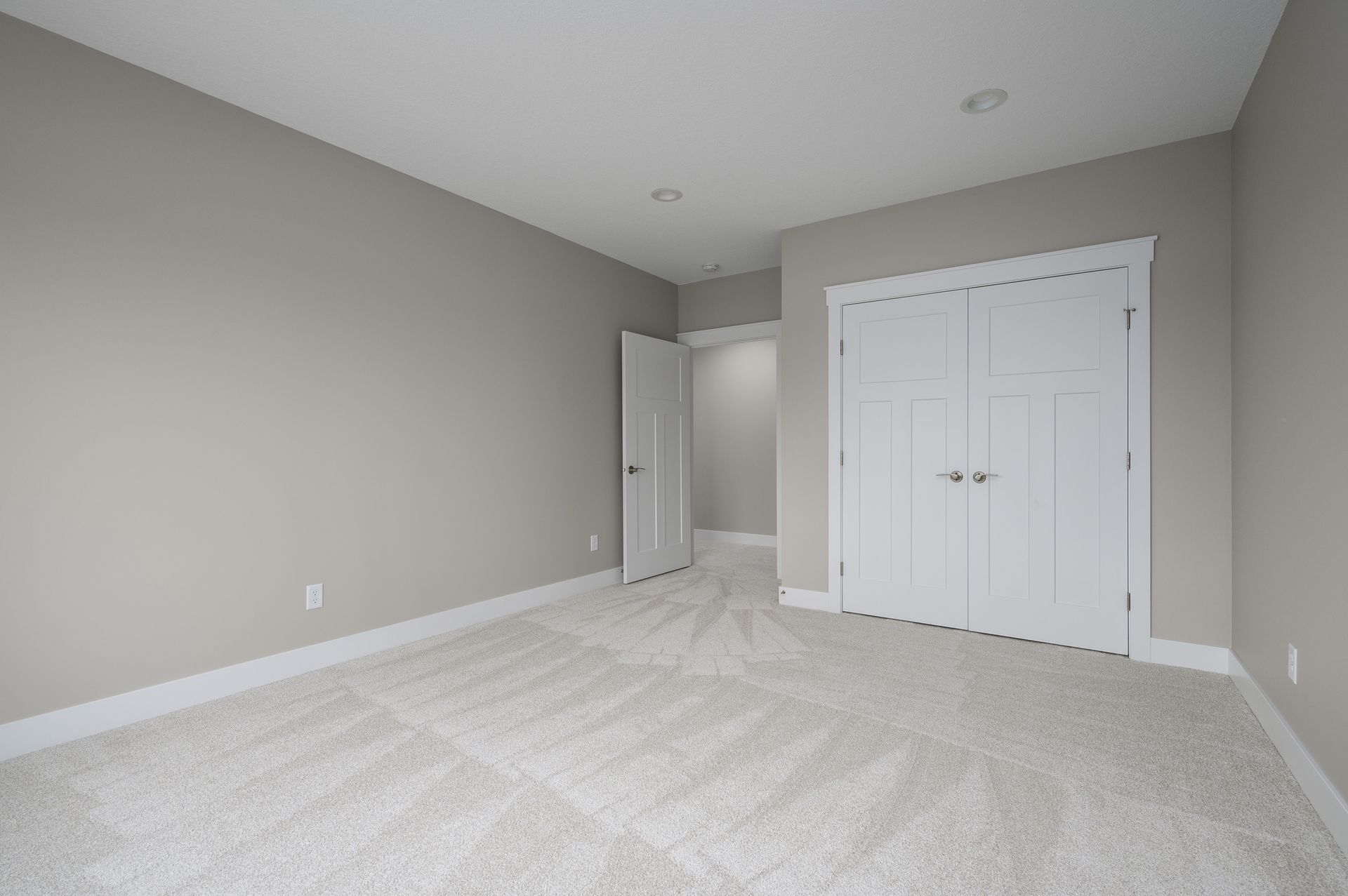 Empty bedroom with gray walls, white trim, and beige carpet. White closet doors.
