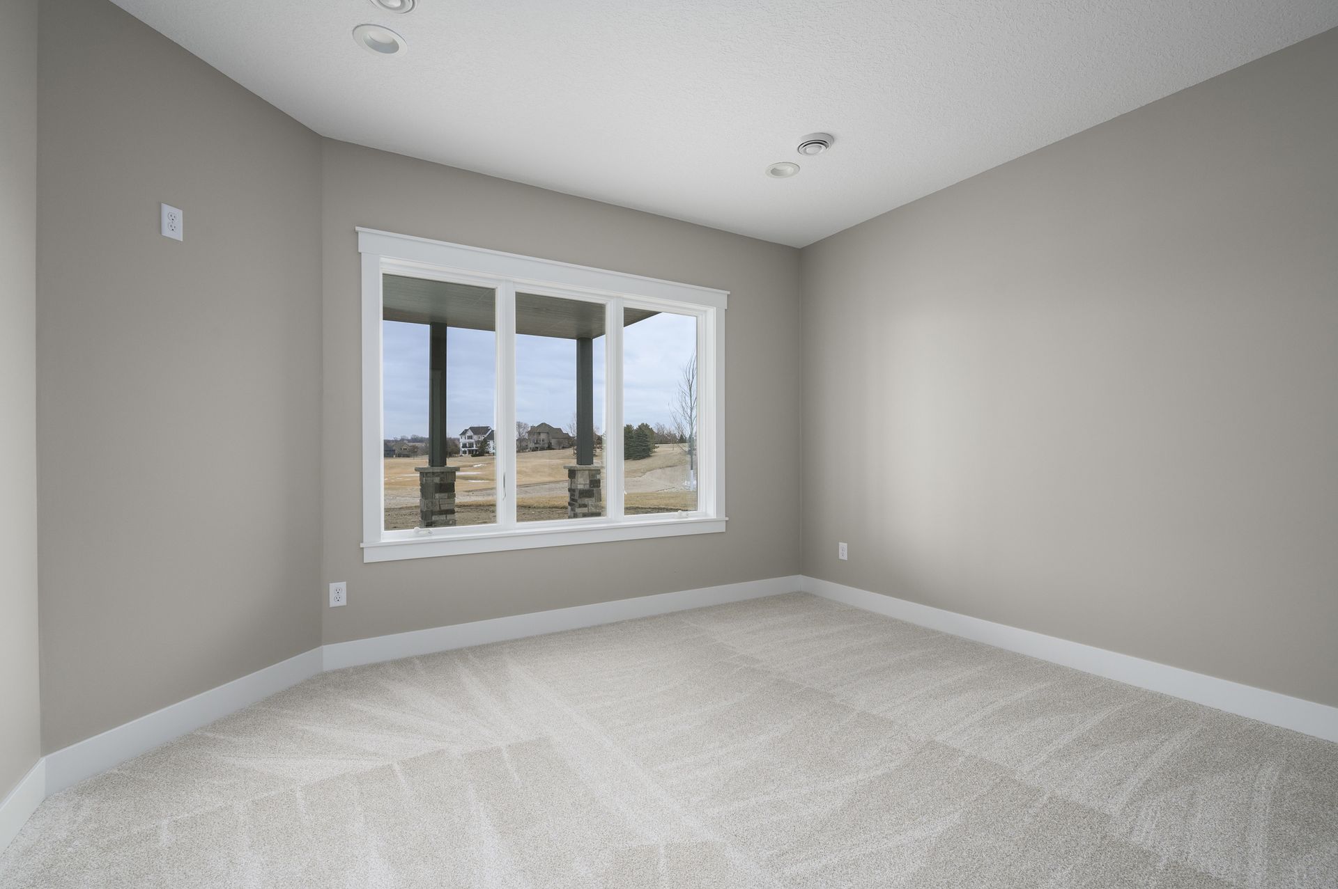 Empty room with beige walls, white trim, and a large window looking outside.