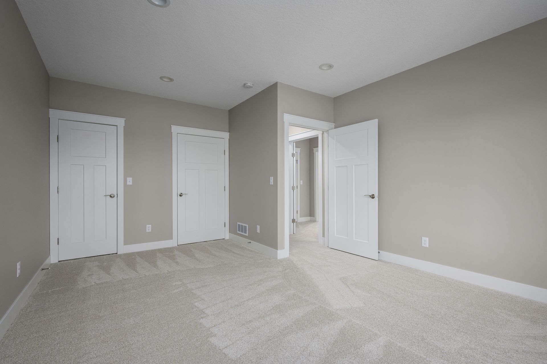 Empty room with neutral walls, white doors, and light carpet flooring.