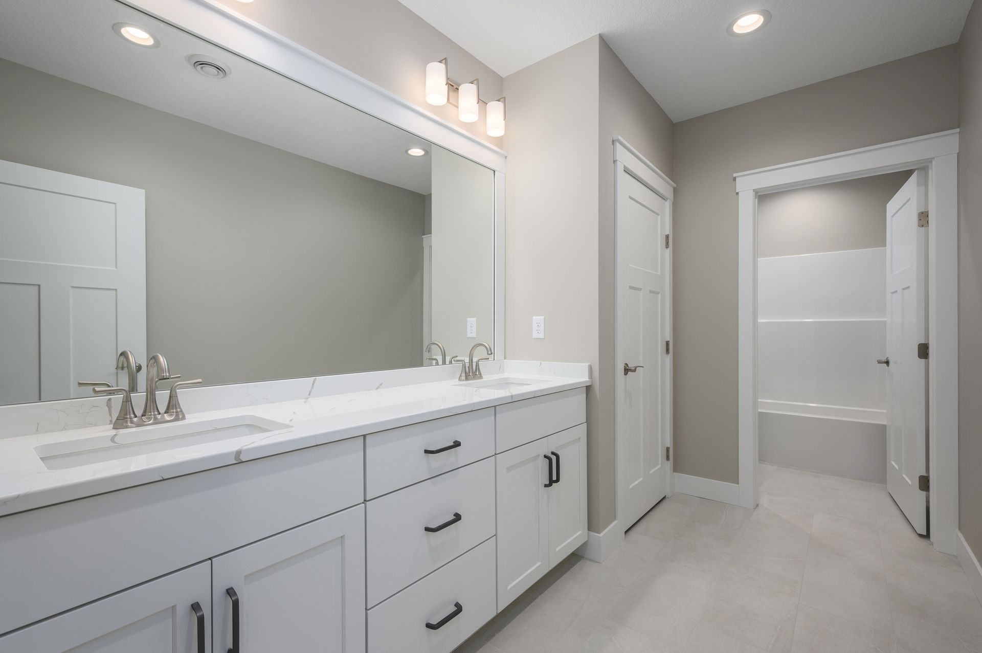 Bathroom with a white double vanity, large mirror, and open door to a bathtub area.