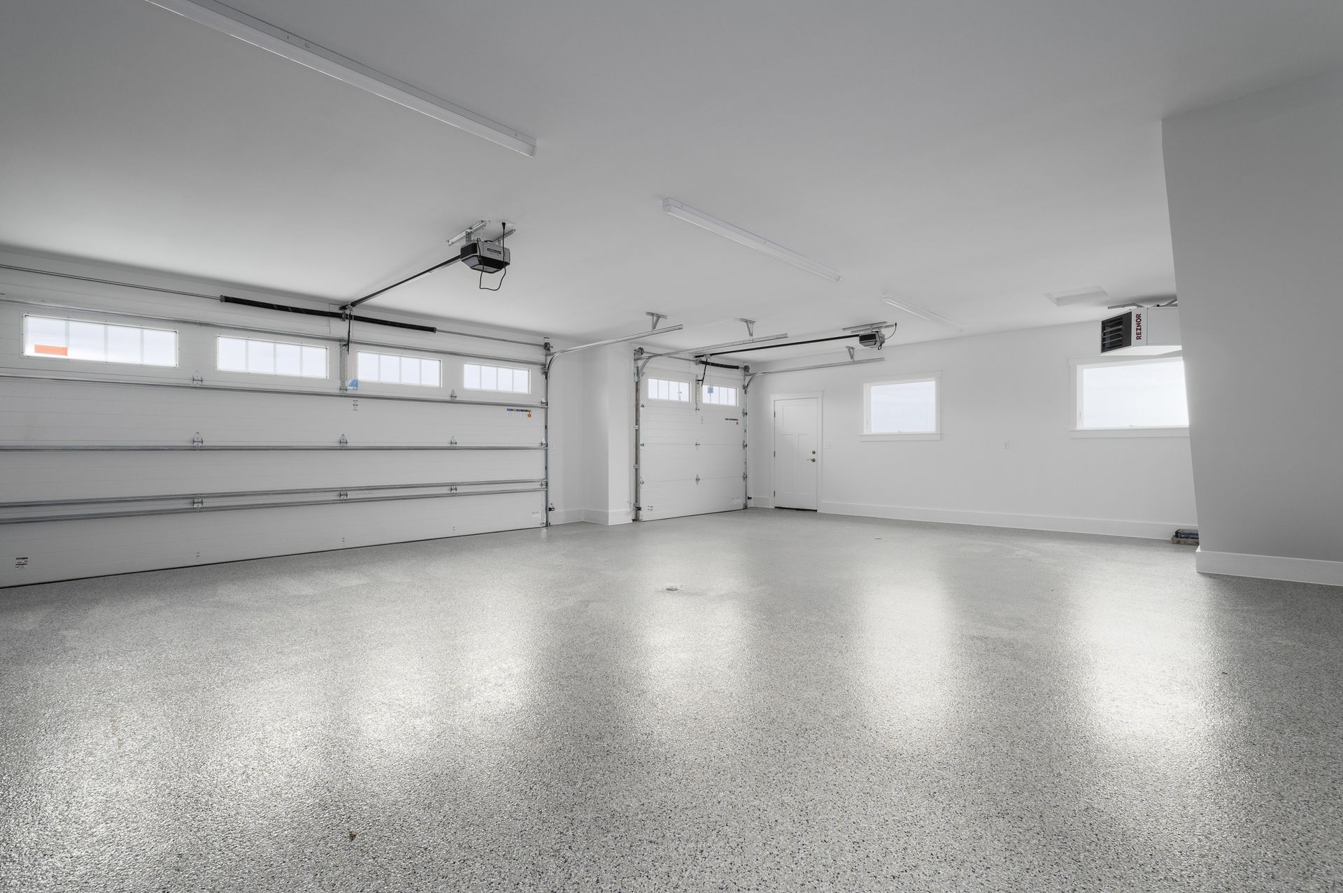Empty garage with shiny, speckled gray floor and white walls. Two garage doors are visible.