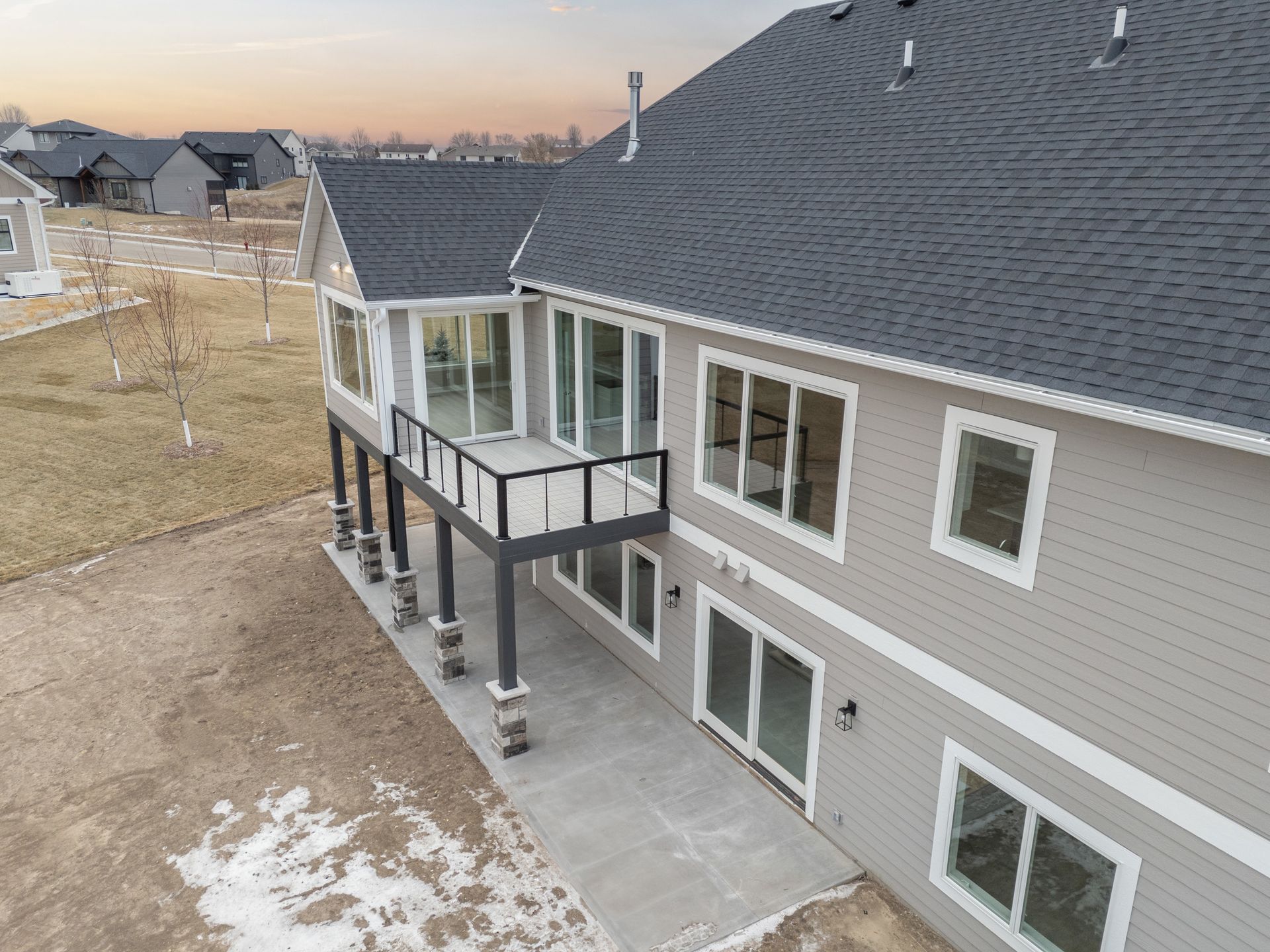 Rear view of a two-story house with a deck. Gray siding, black roof, and large windows.