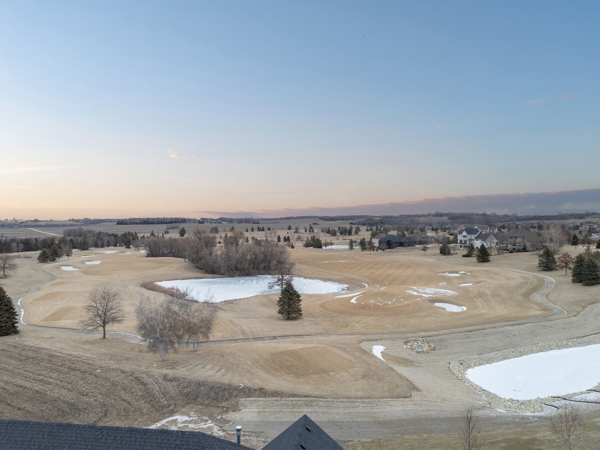 Overhead view of a golf course, patches of snow, brown grass, and a blue sky.