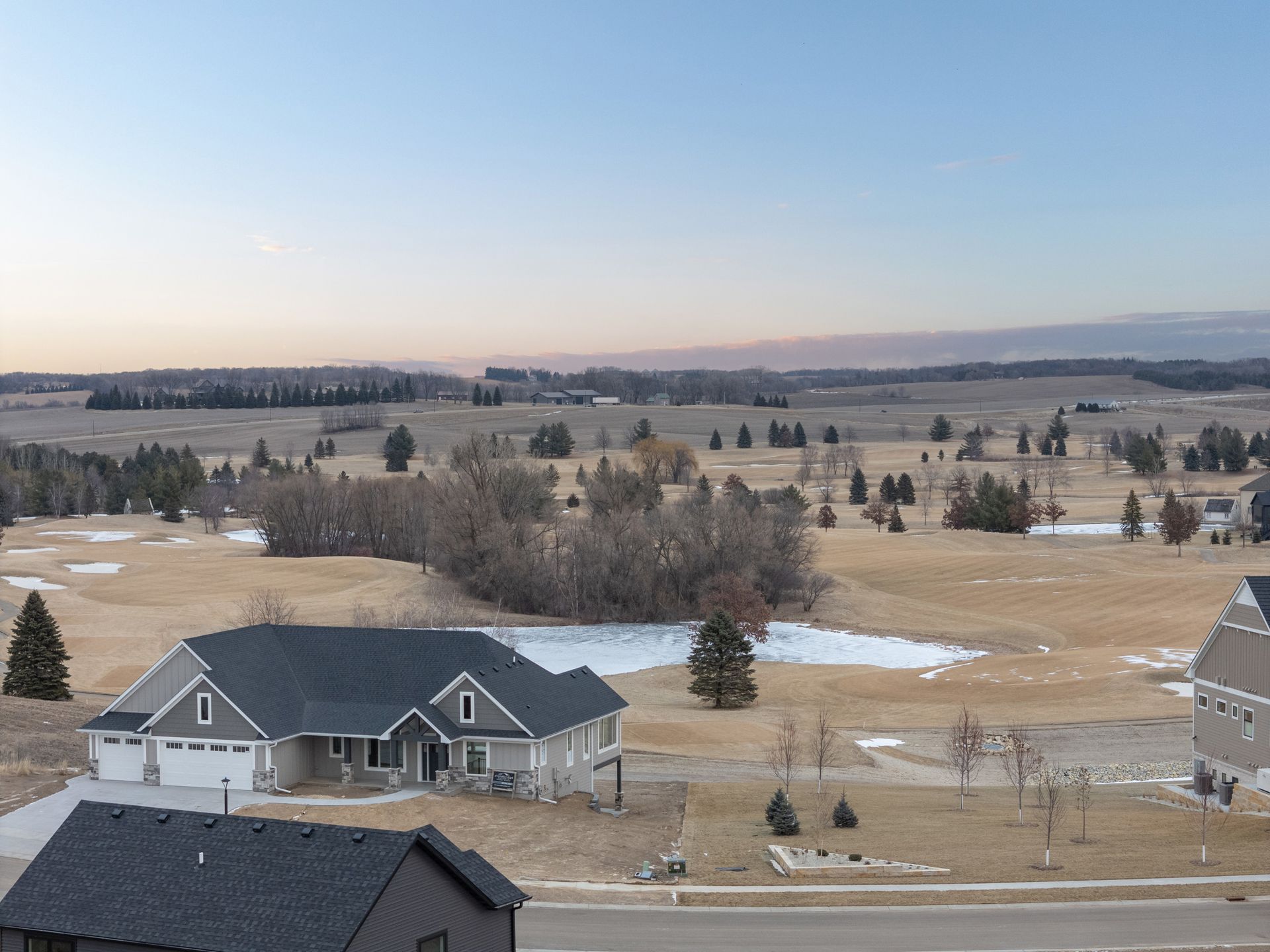 A house overlooks a golf course under a pastel sky.