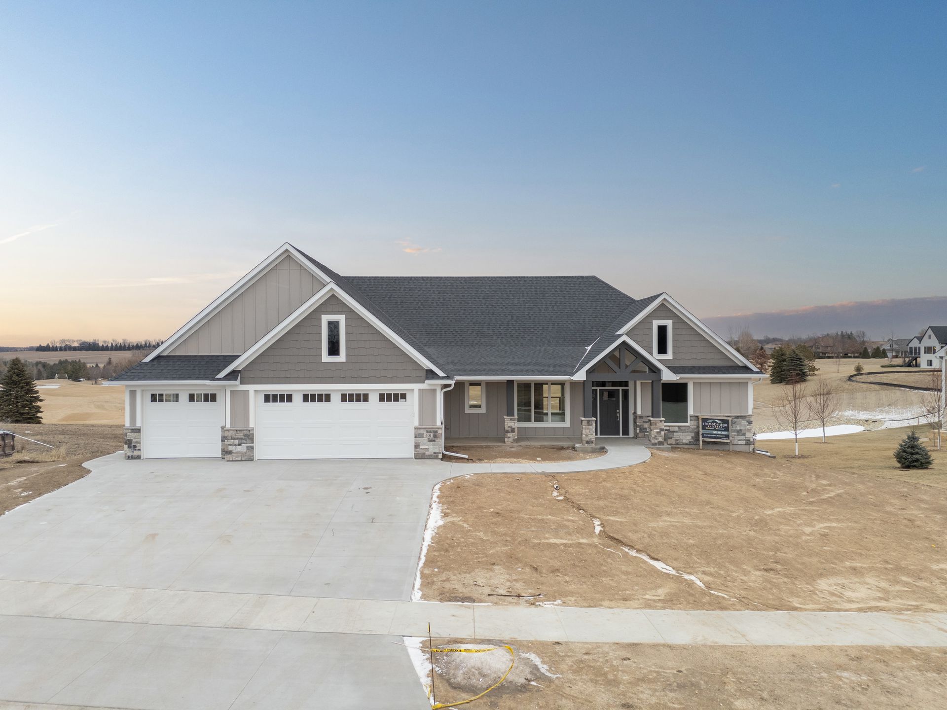 Gray house with a two-car garage, stone accents, and a long driveway under a clear sky.