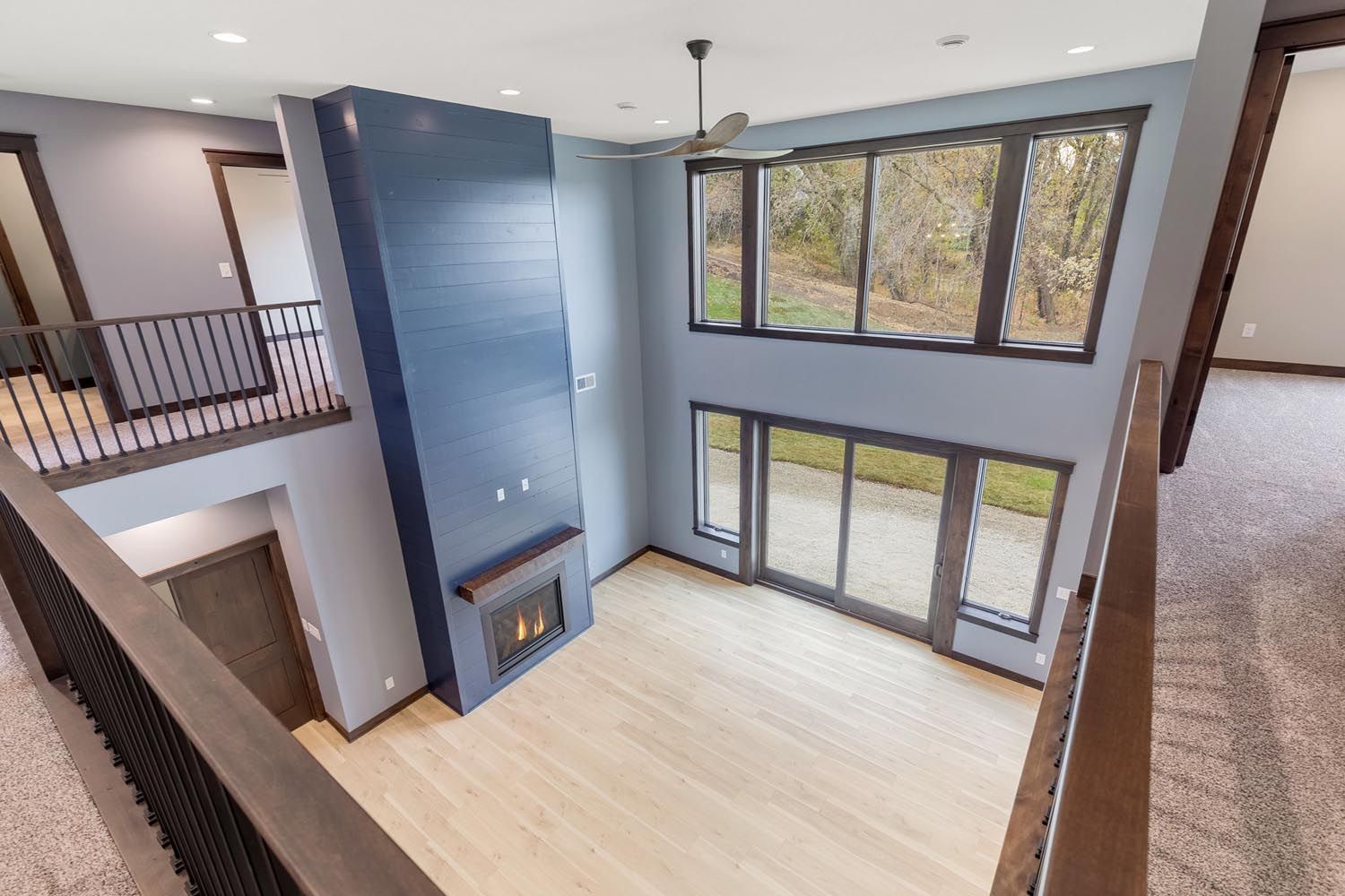 Two-story living room with blue walls, fireplace, balcony, large windows, and light wood floors.