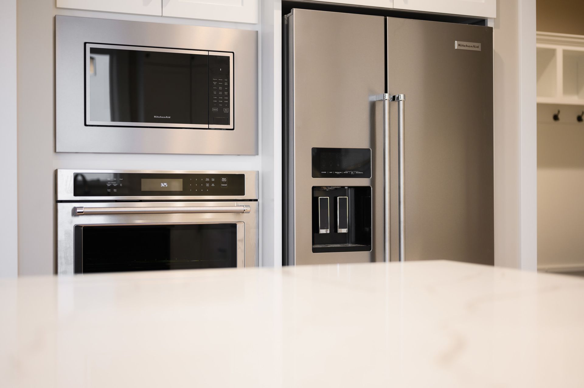 Stainless steel microwave and oven built into a kitchen wall, next to a stainless steel refrigerator.