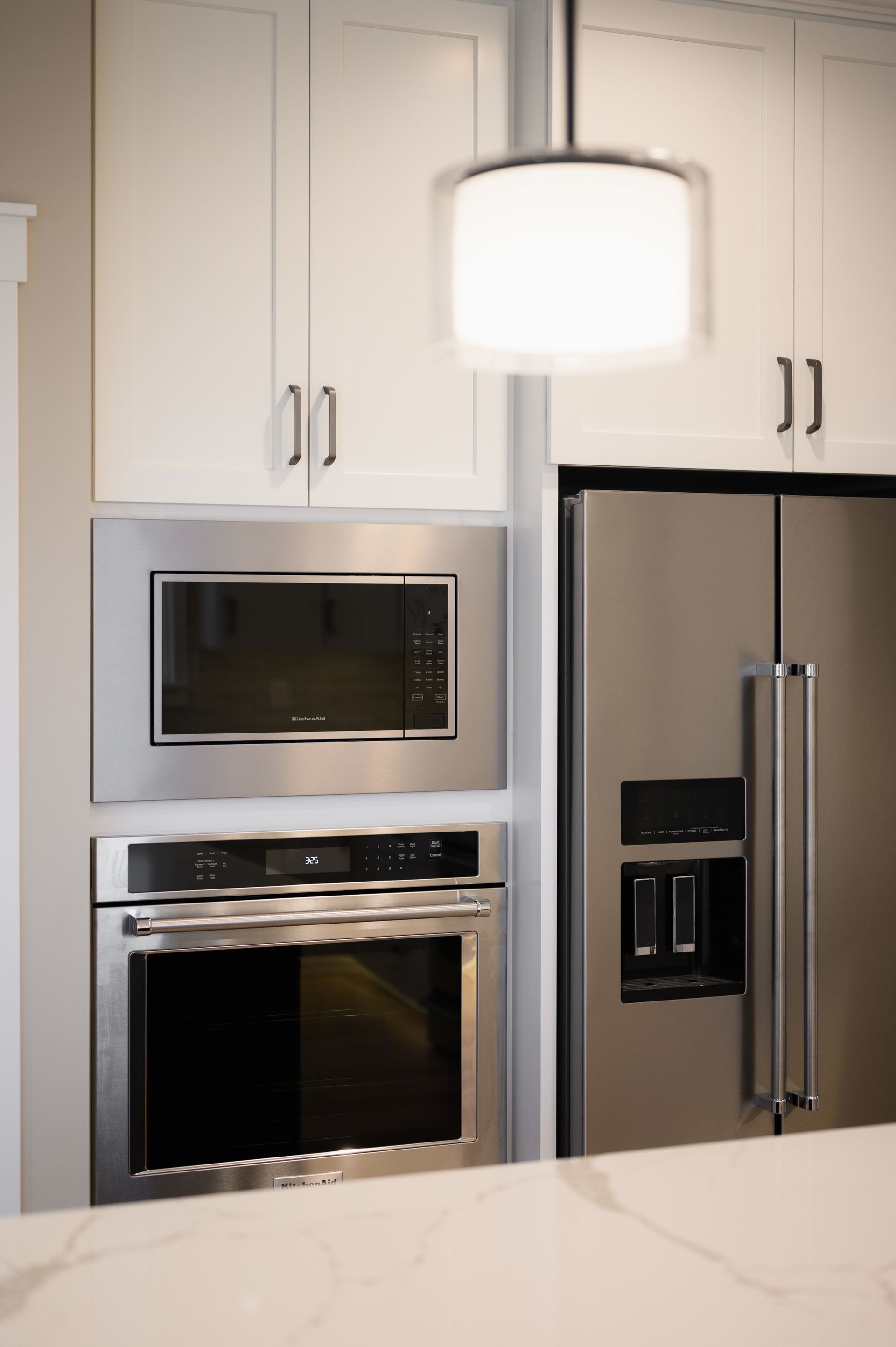 Stainless steel oven and microwave built into white cabinets, next to a refrigerator.