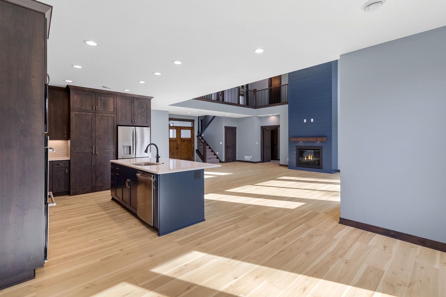 Open-concept kitchen and living area with hardwood floors, dark cabinets, blue accent walls, and a fireplace.