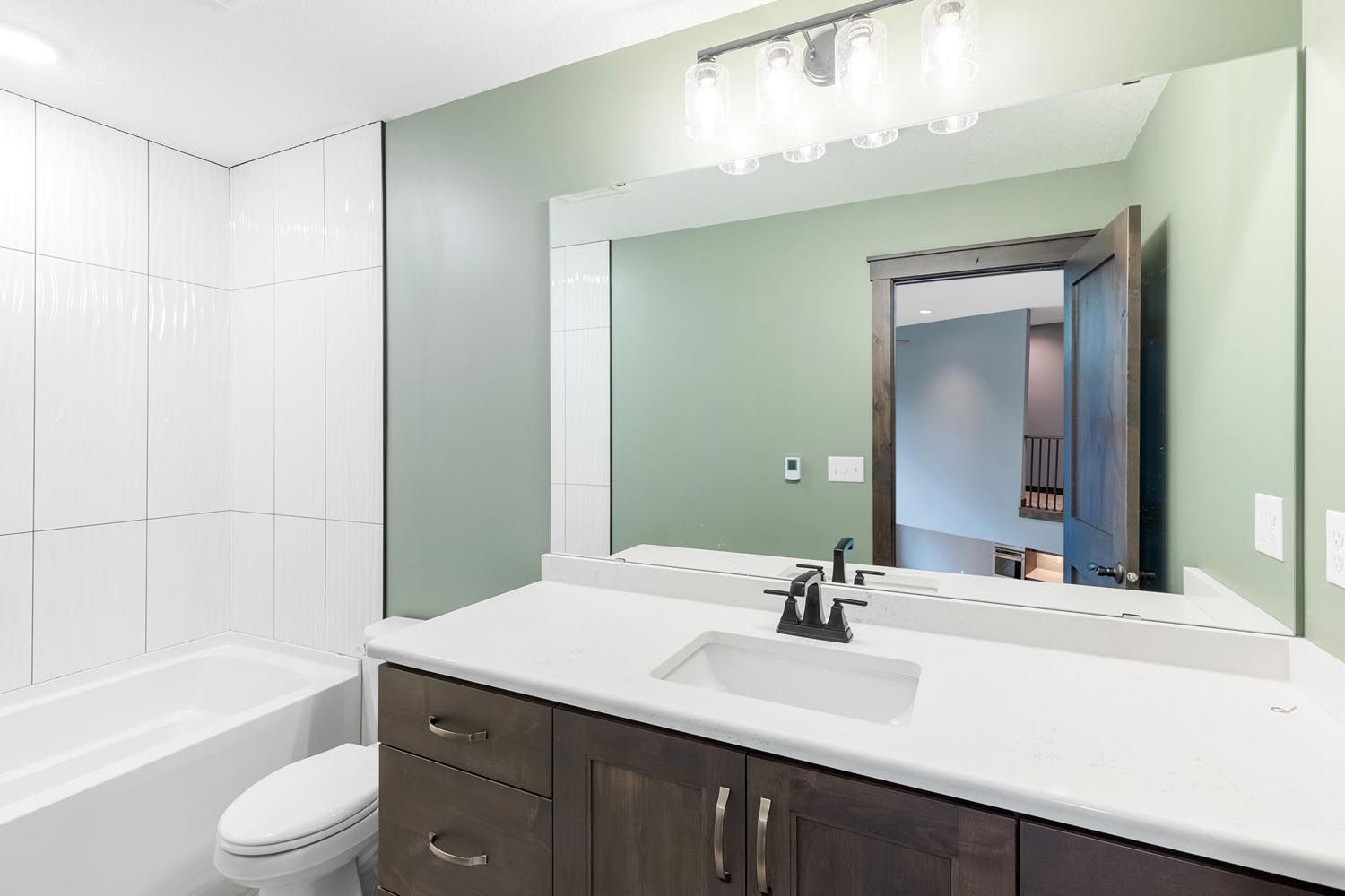 Bathroom with white countertop, dark cabinets, large mirror, and green walls.