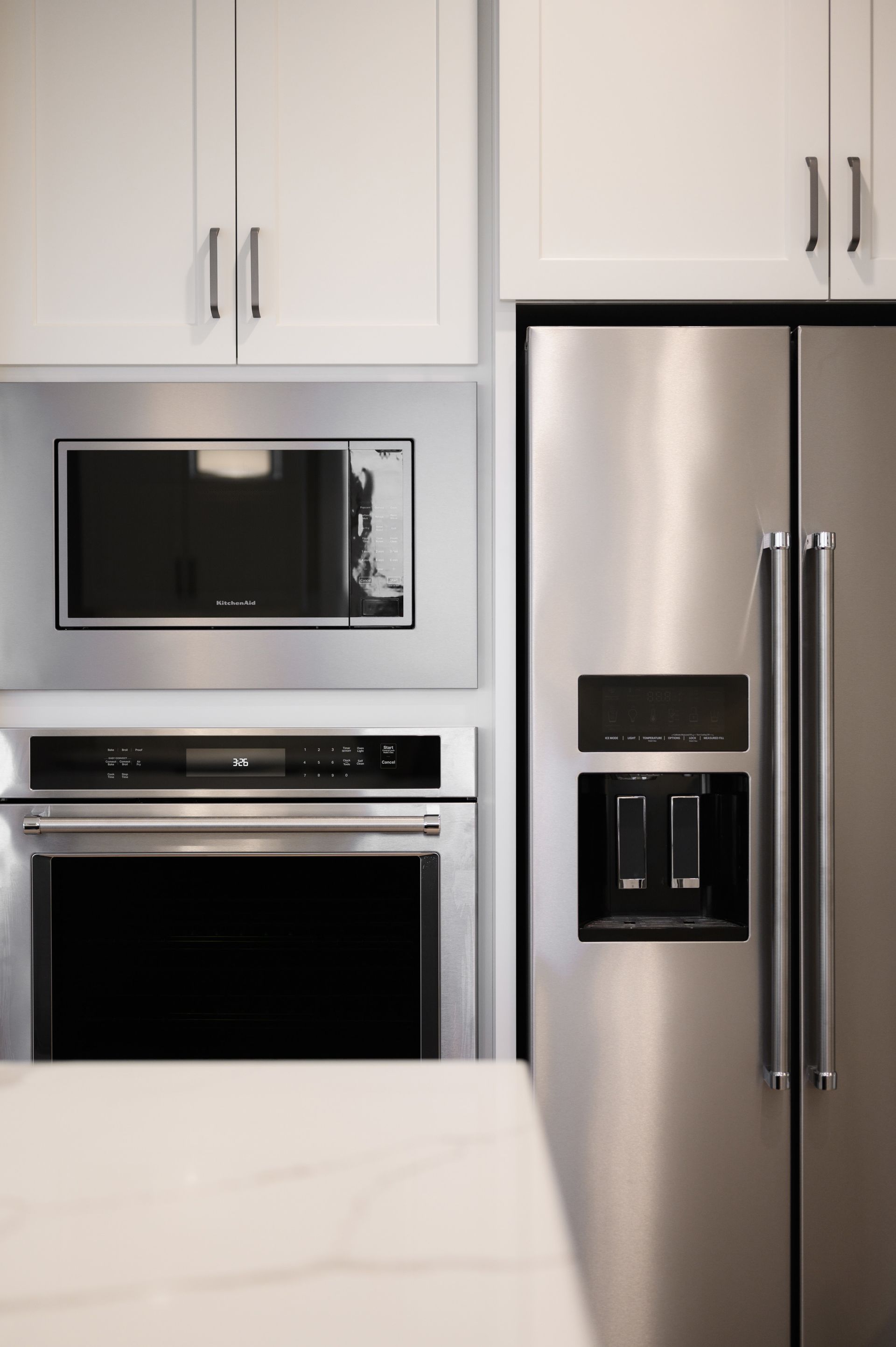 Stainless steel kitchen appliances: microwave, oven, and refrigerator next to white cabinets.