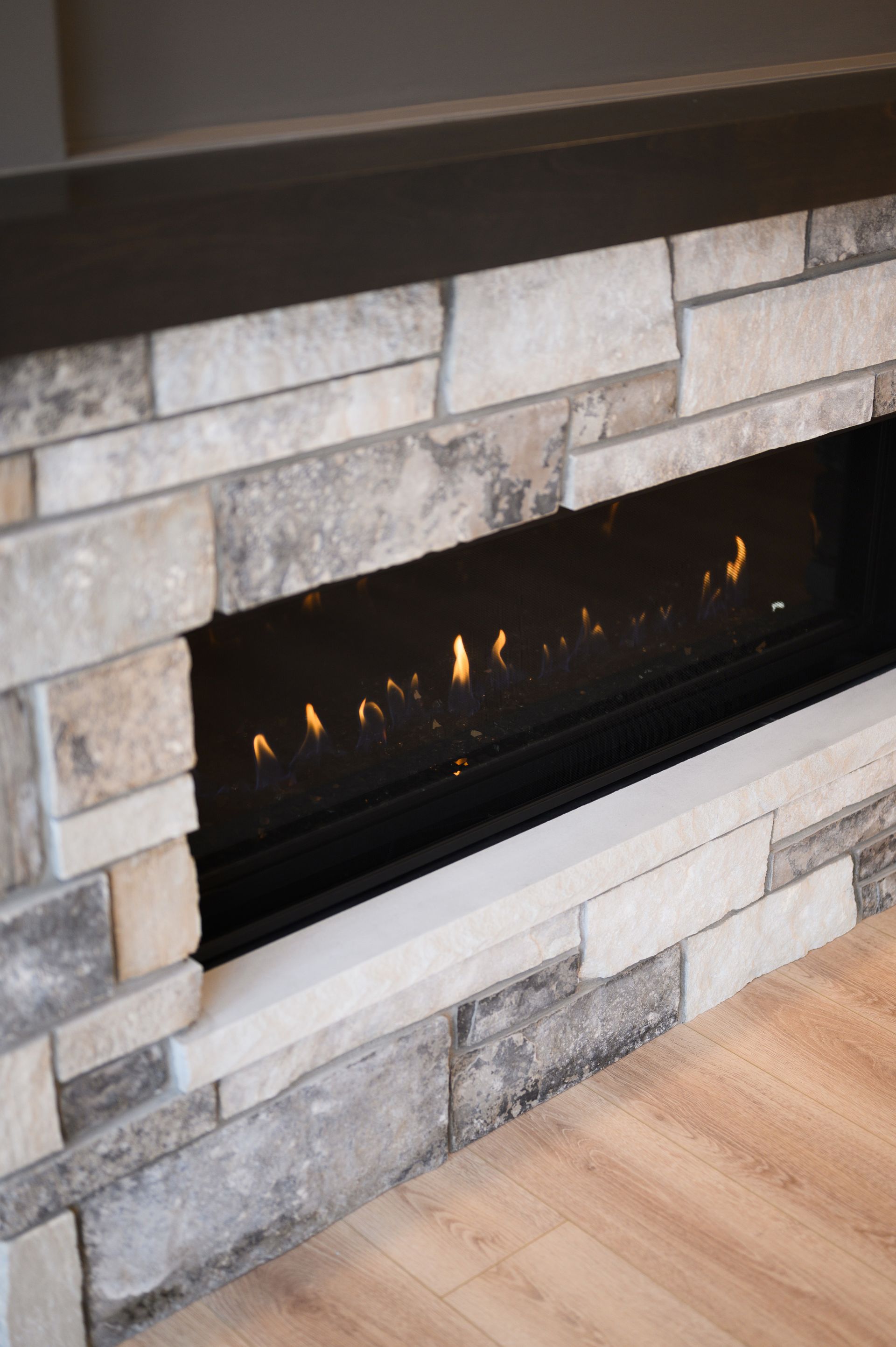 Fireplace with burning flames, surrounded by stone and a dark top, set on a wooden floor.