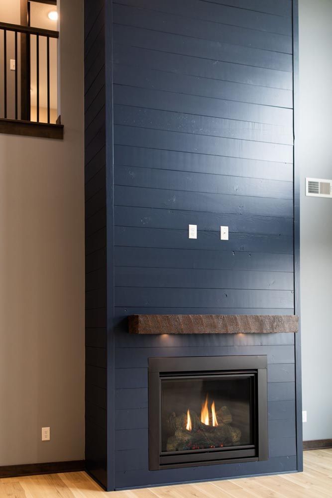 Navy blue shiplap fireplace with a rustic wooden mantel and a lit fire, in a modern interior.