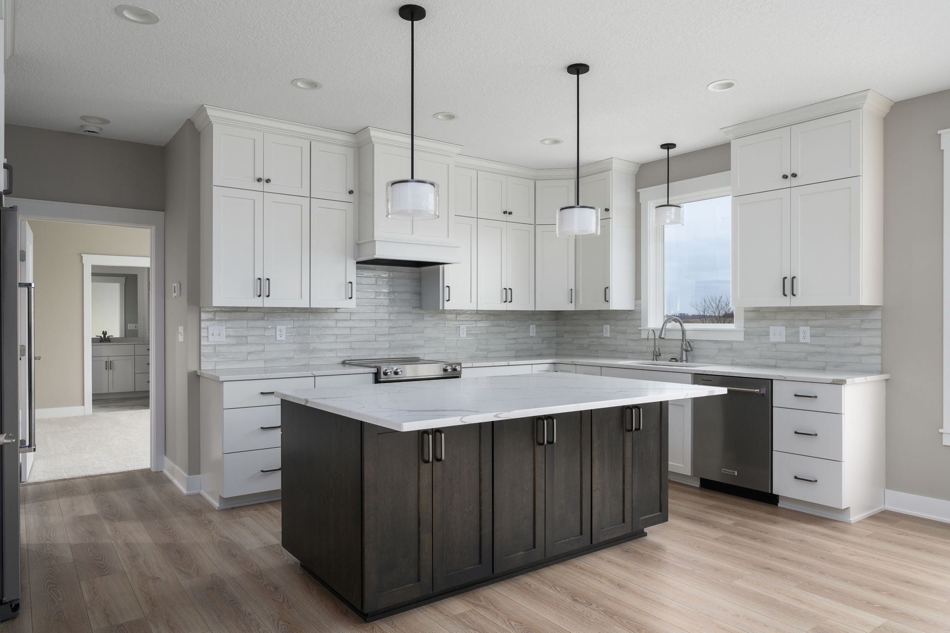 Modern kitchen with white cabinets, dark island, and stainless steel appliances.