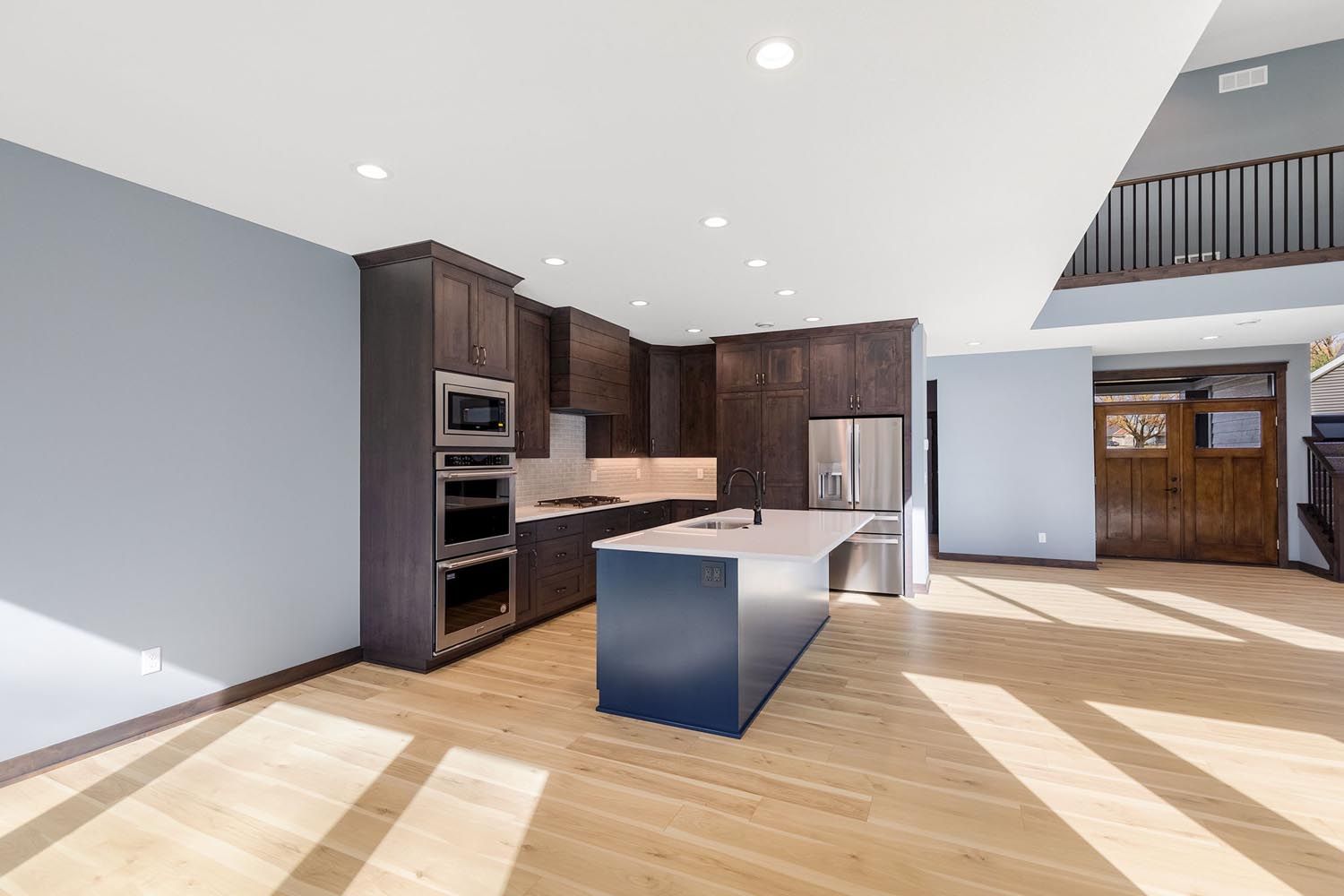 Modern kitchen with blue island and cabinets, stainless steel appliances, and wooden floors.