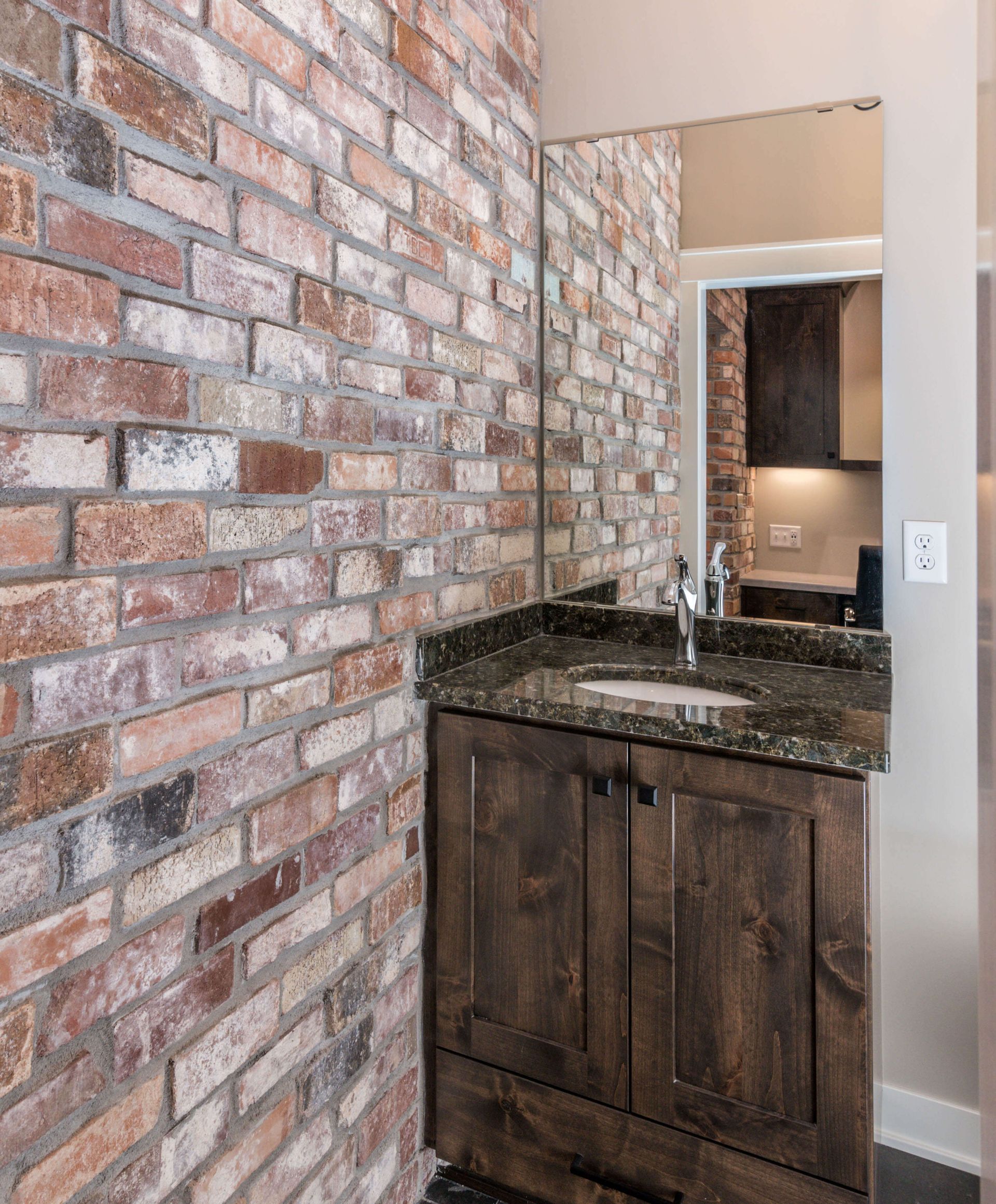 Bathroom with exposed brick wall, dark wood vanity, granite countertop, and mirror.