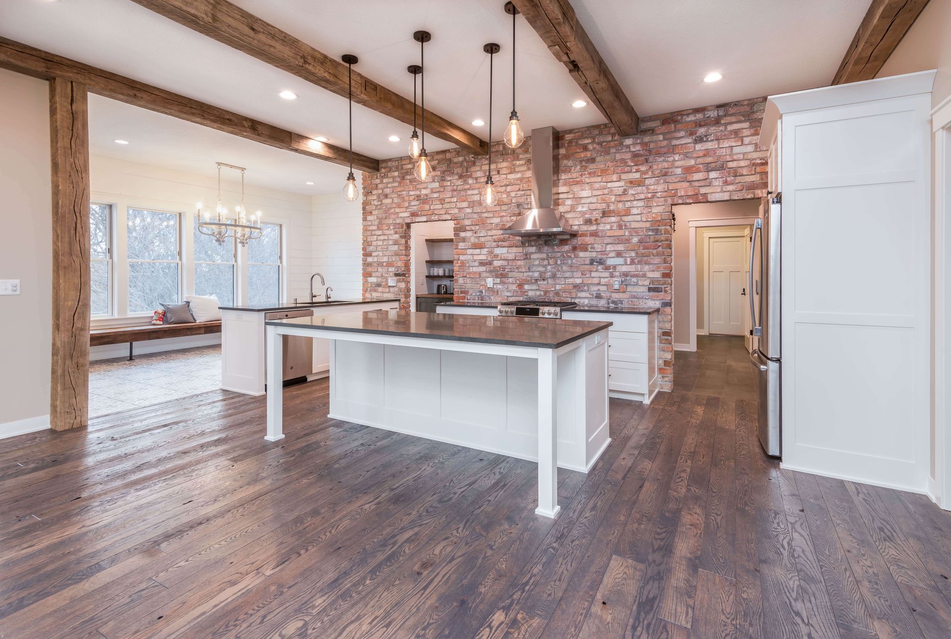 Kitchen with brick accent wall, white cabinets, island, and wooden beams. Dark wood floor.