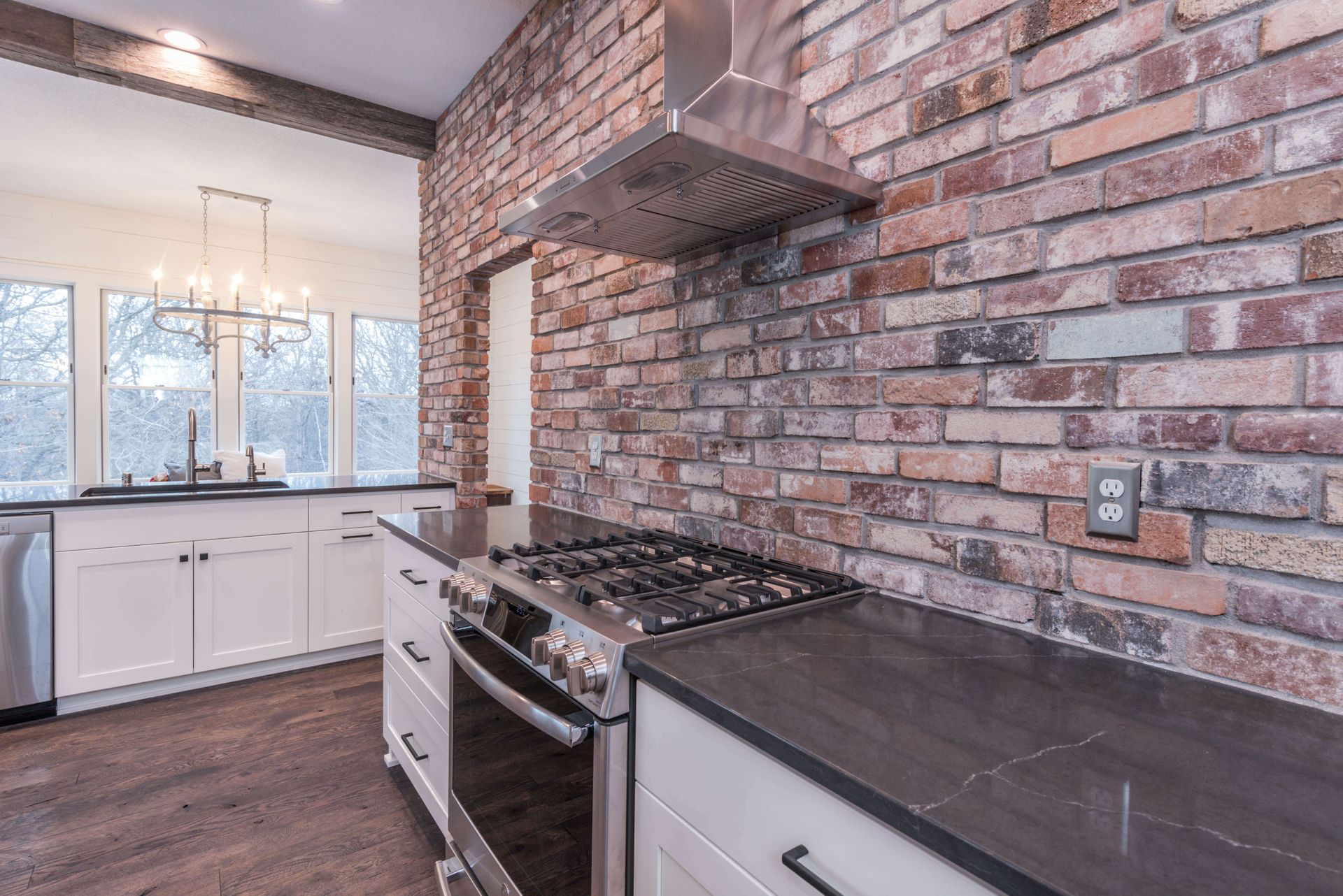 Kitchen with brick wall, stainless steel range, and white cabinets.