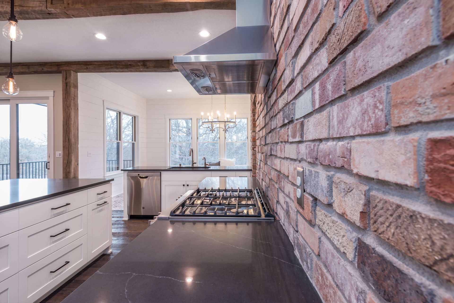 Kitchen with brick accent wall, stainless steel appliances, dark countertop, and white cabinets.