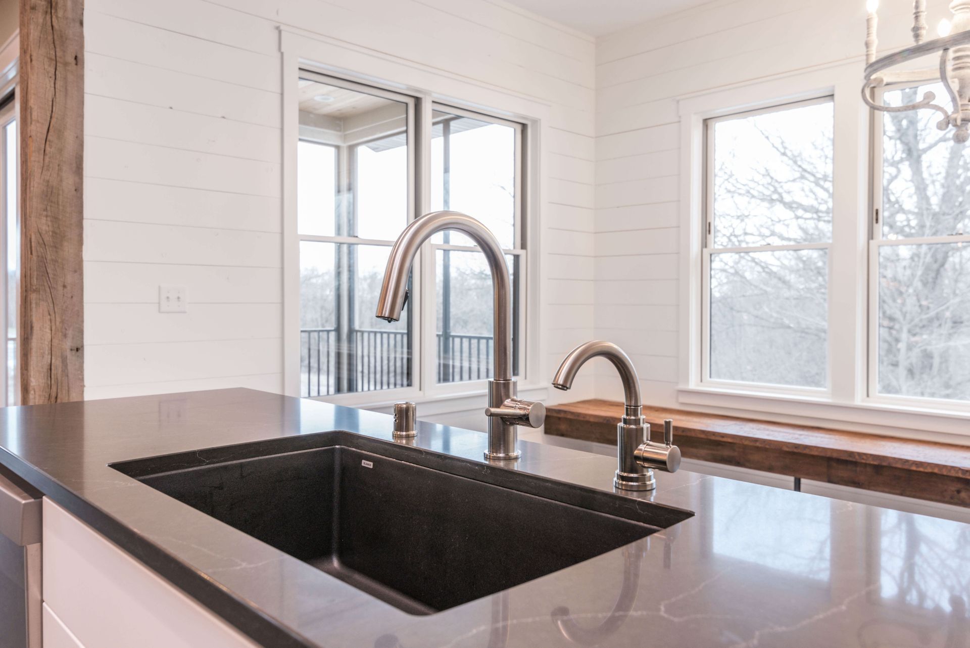 Kitchen sink with a tall faucet, set against a backdrop of white shiplap walls and windows overlooking trees.