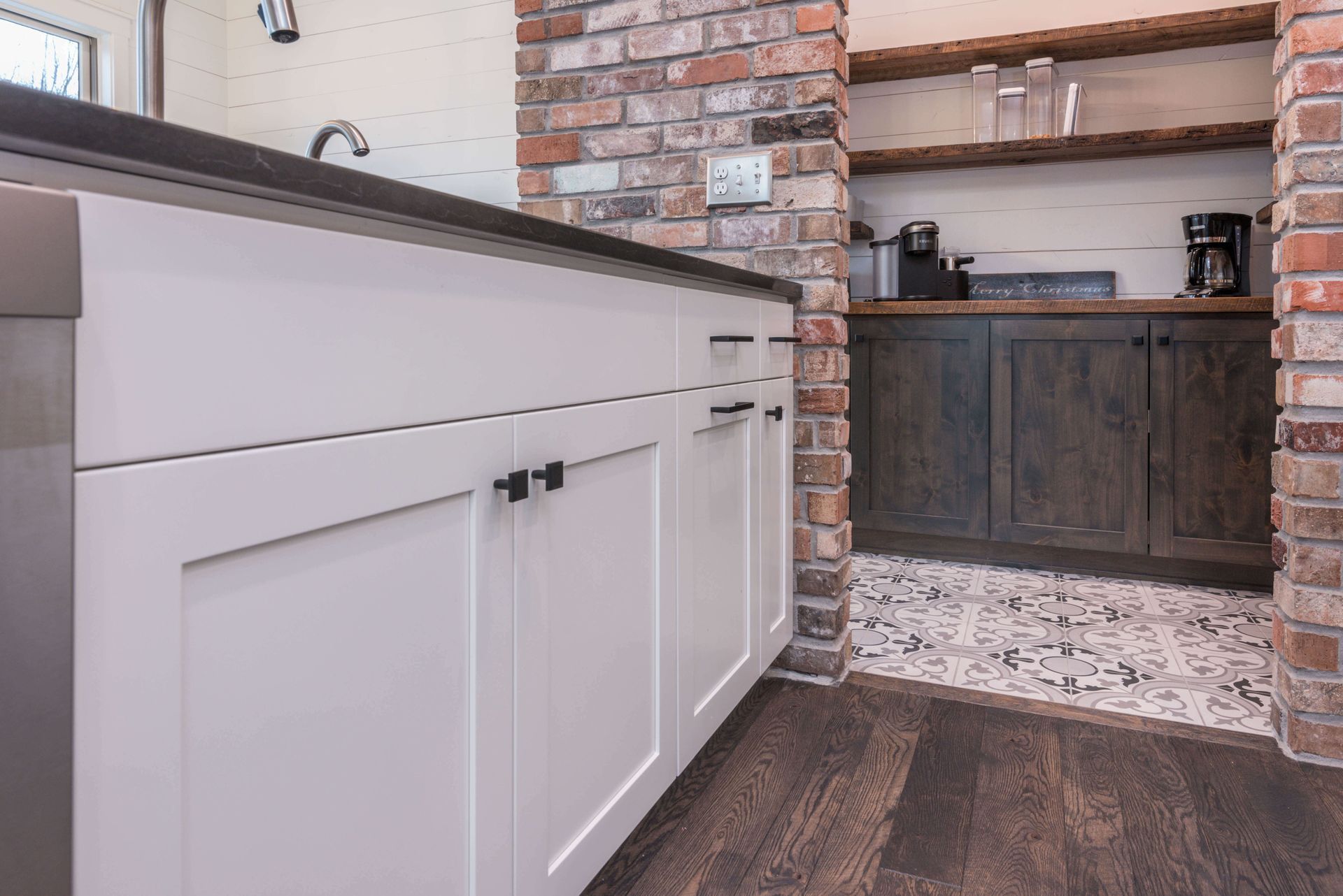White kitchen cabinets with black hardware, brick accent, and dark wood flooring.
