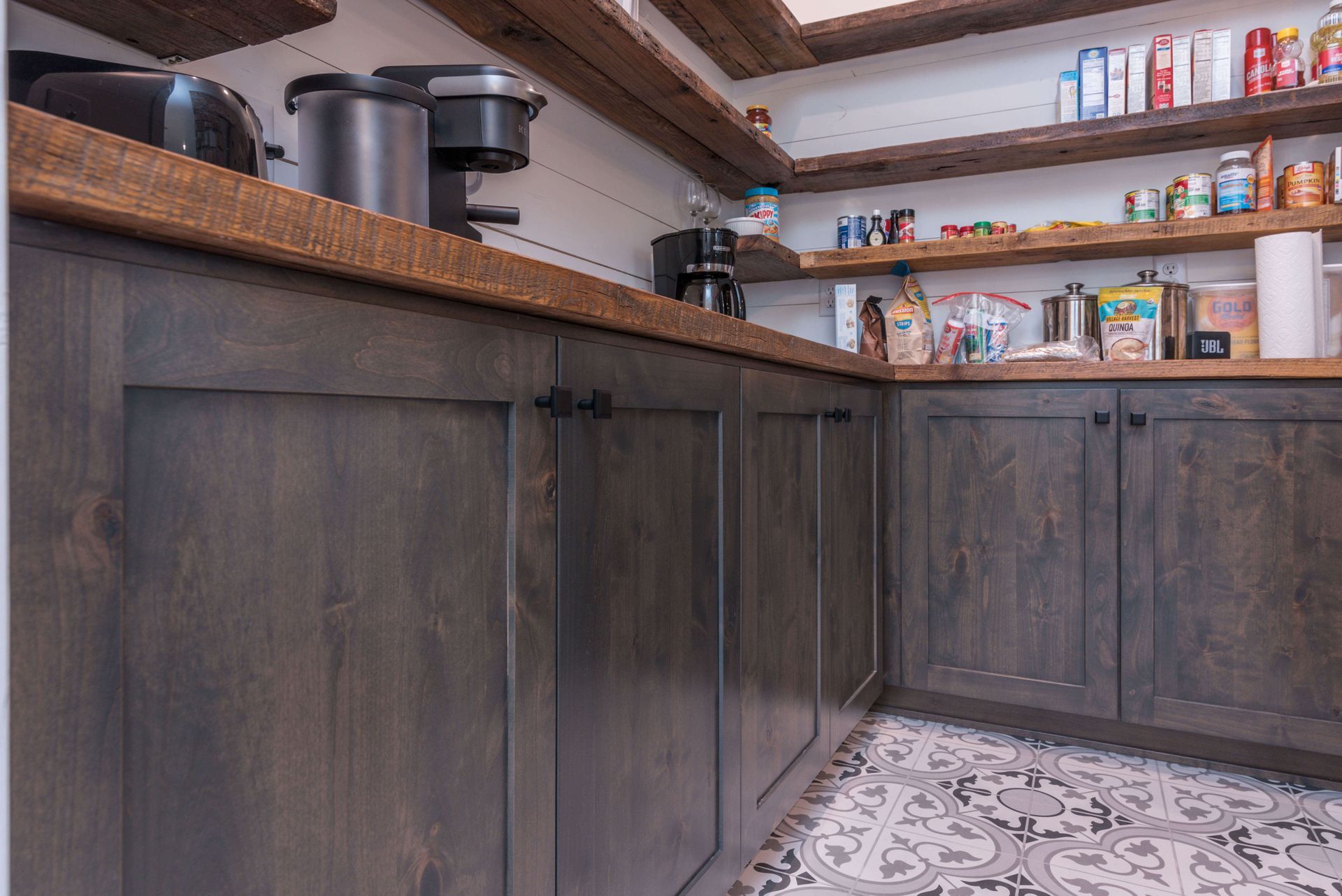 Dark gray kitchen cabinets with a wooden countertop and shelves stocked with canned goods.