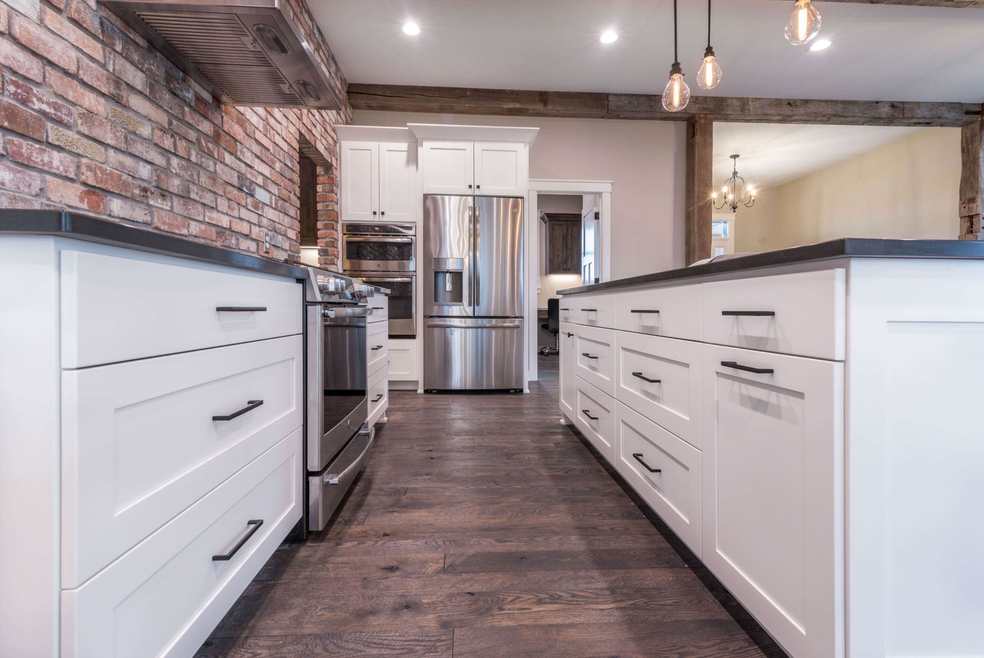 White kitchen with dark countertops, brick wall, stainless steel appliances, and wood floor.